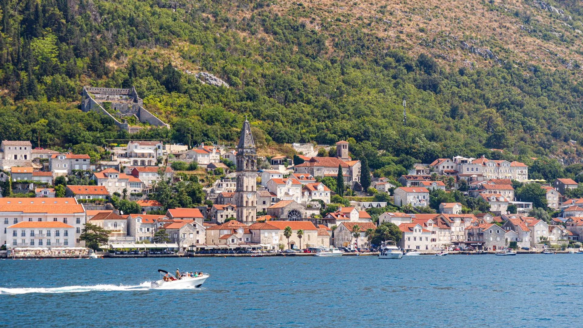 Perast's stone waterfront and church tower beside the blue Bay of Kotor in bright daylight