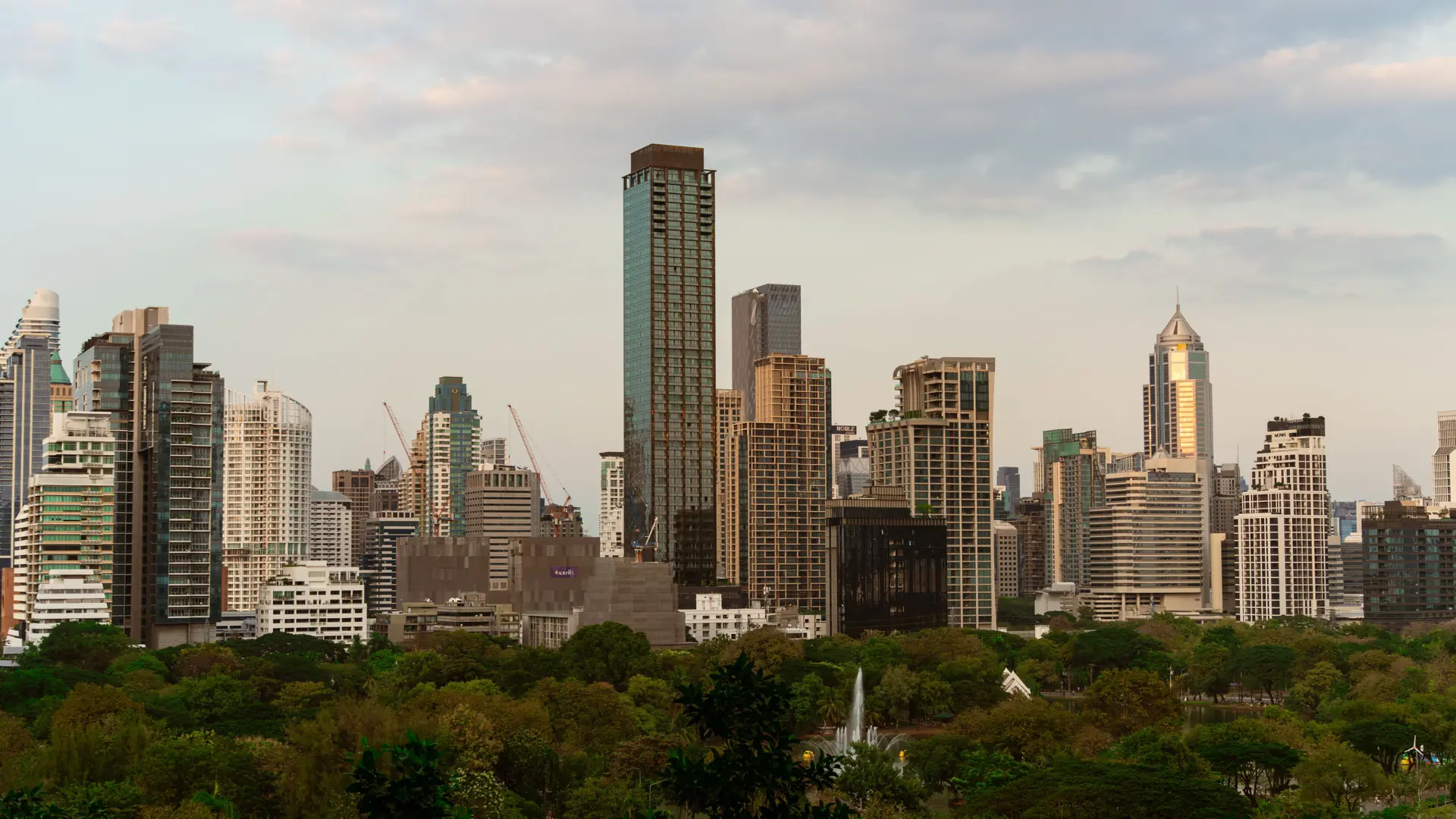 Bangkok's modern Sukhumvit skyline glowing beyond treetops at dusk