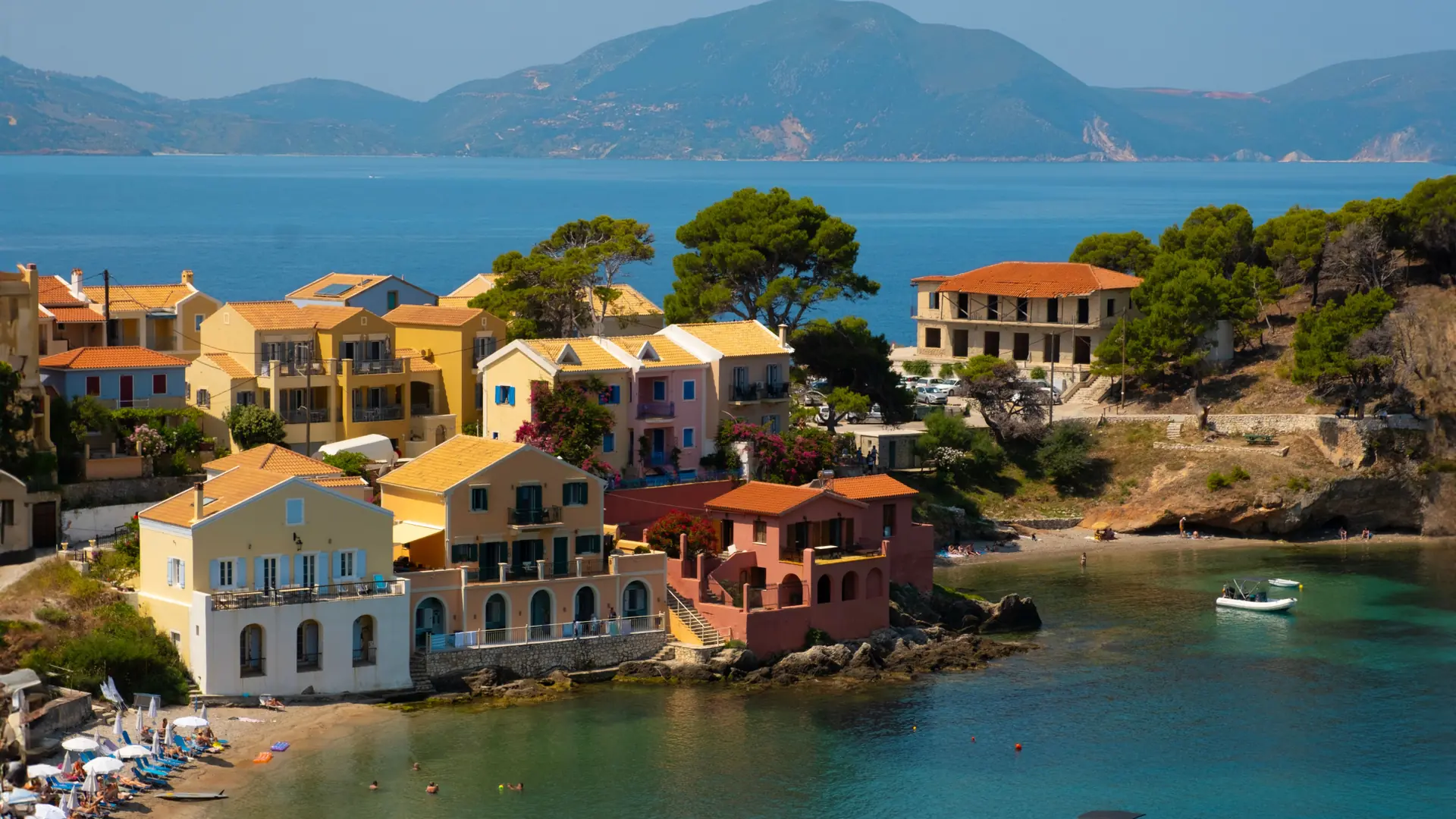 Colourful houses around Assos harbour with turquoise water and Kefalonian hills beyond