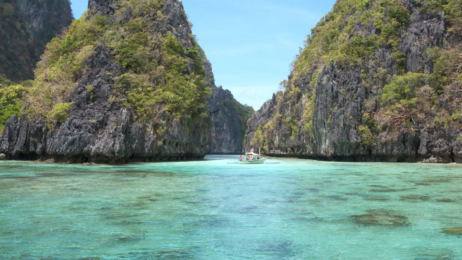 Turquoise water between limestone cliffs in Bacuit Bay, El Nido, beneath a blue sky