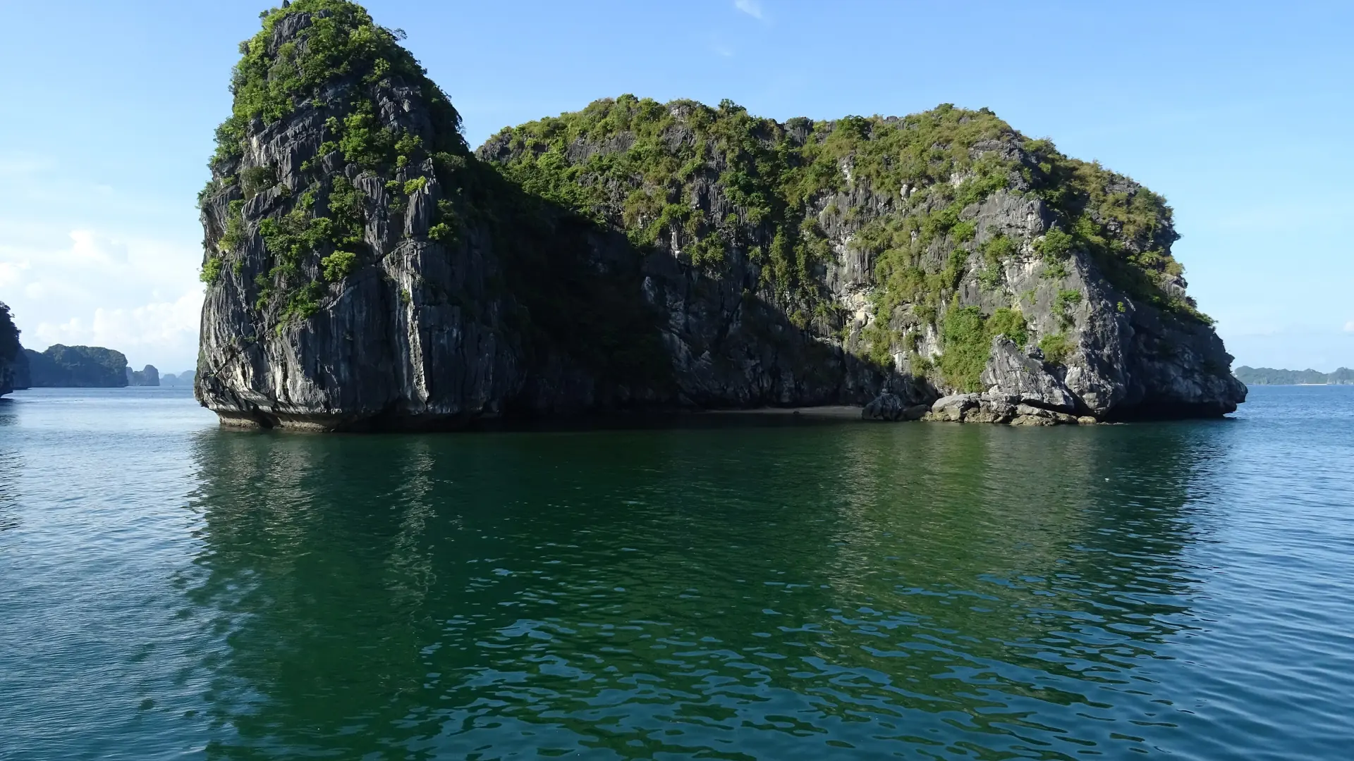 A green limestone island reflected in calm water in Ha Long Bay.
