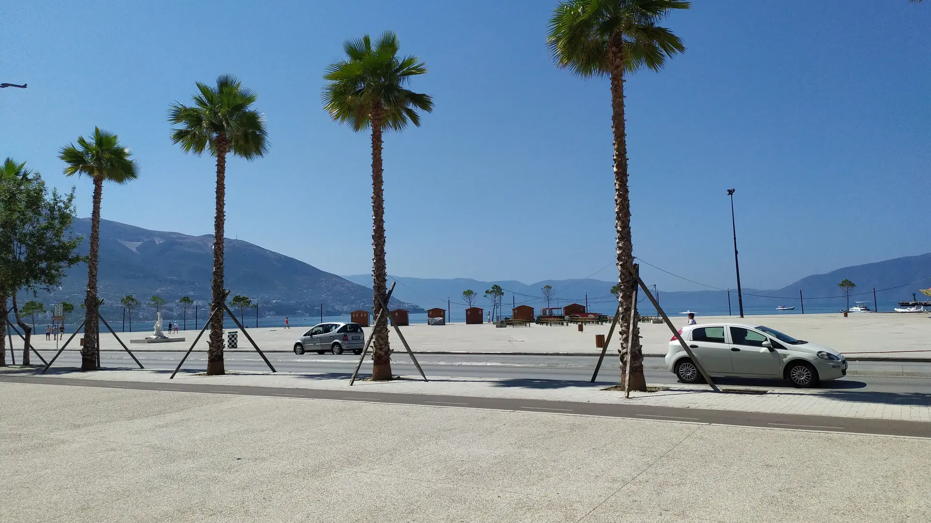 Palm-lined promenade and beach along Vlorë's Lungomare with the bay beyond on a bright day