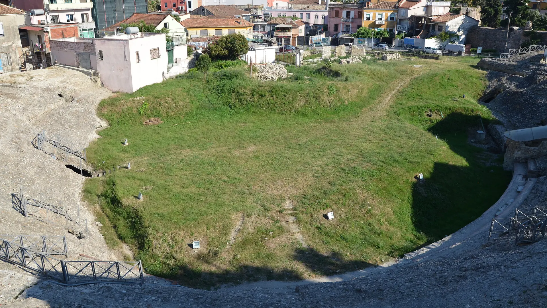The grassy arena of the Roman amphitheatre in Durrës, ringed by the modern city on a sunny day