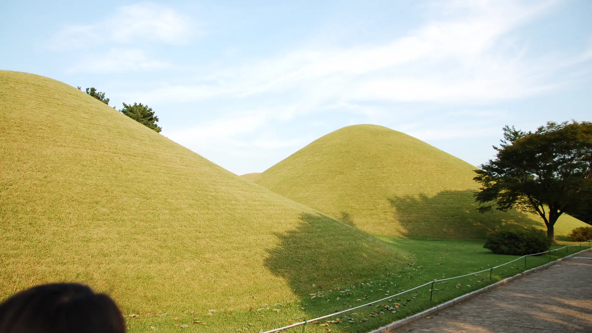 Grass-covered royal tomb mounds in Gyeongju's Daereungwon complex under a bright blue sky