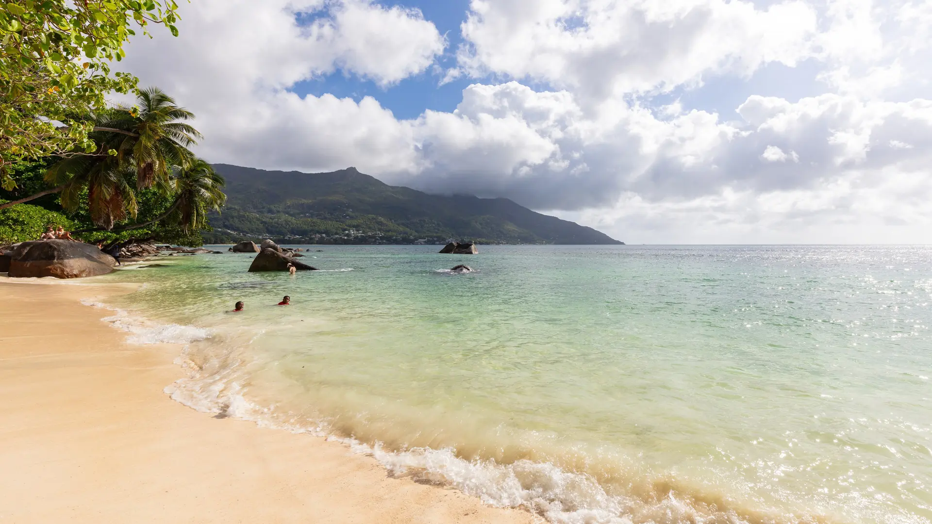 Pale sand and shallow turquoise water below green hills at Beau Vallon, Mahé