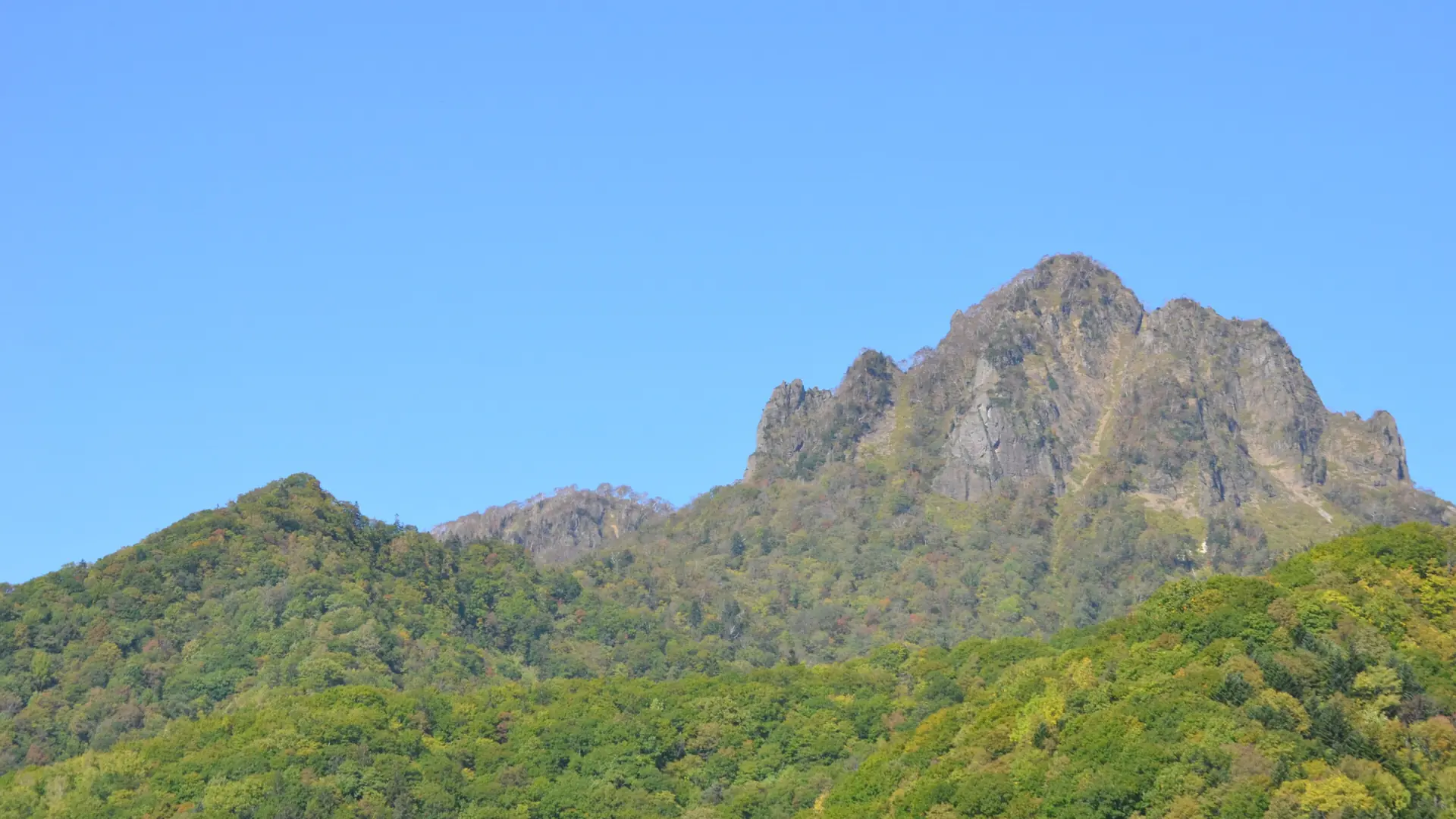 The rocky summit of Mount Tengu above the wooded Jozankei slopes in daylight