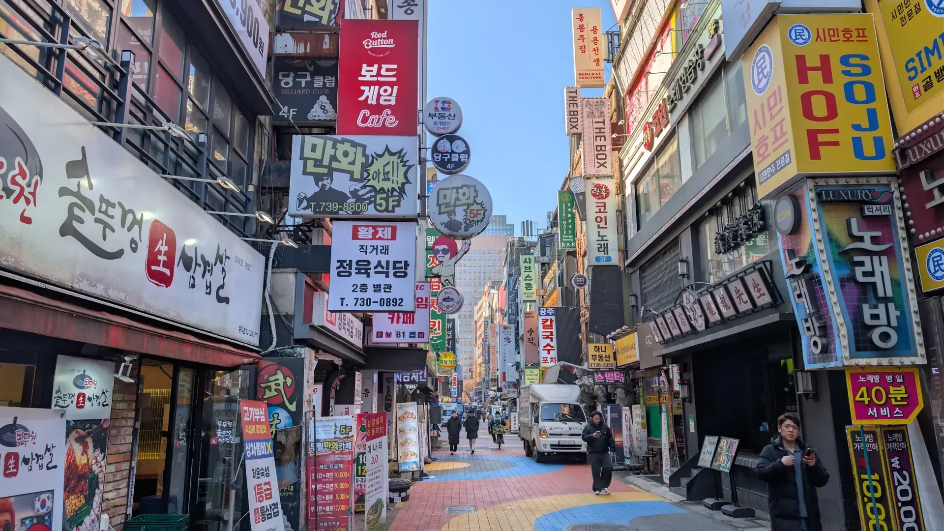 Shops and signs along a busy Seoul street in daylight