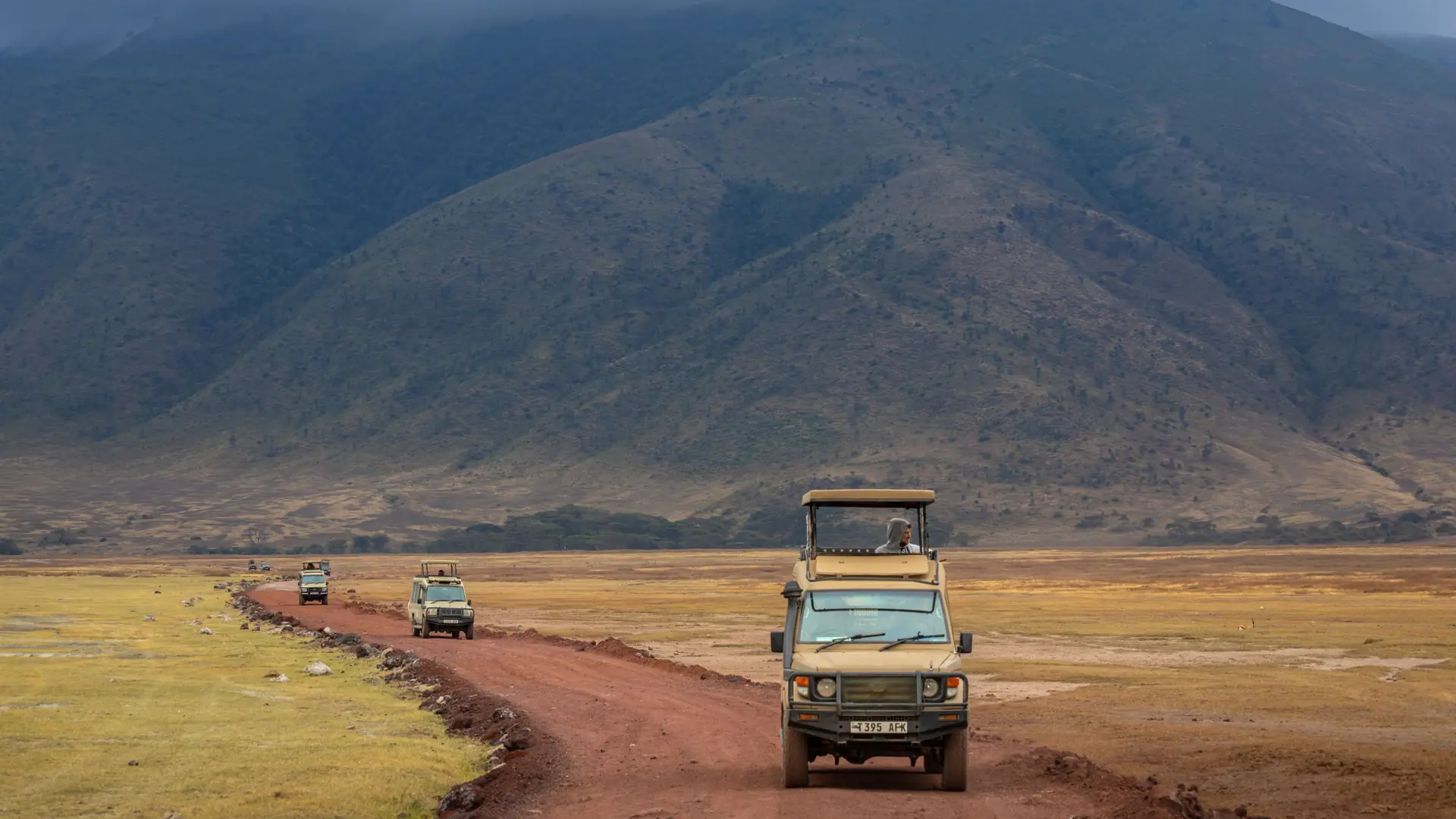 Safari vehicles driving a dirt track through Ngorongoro Crater in daylight