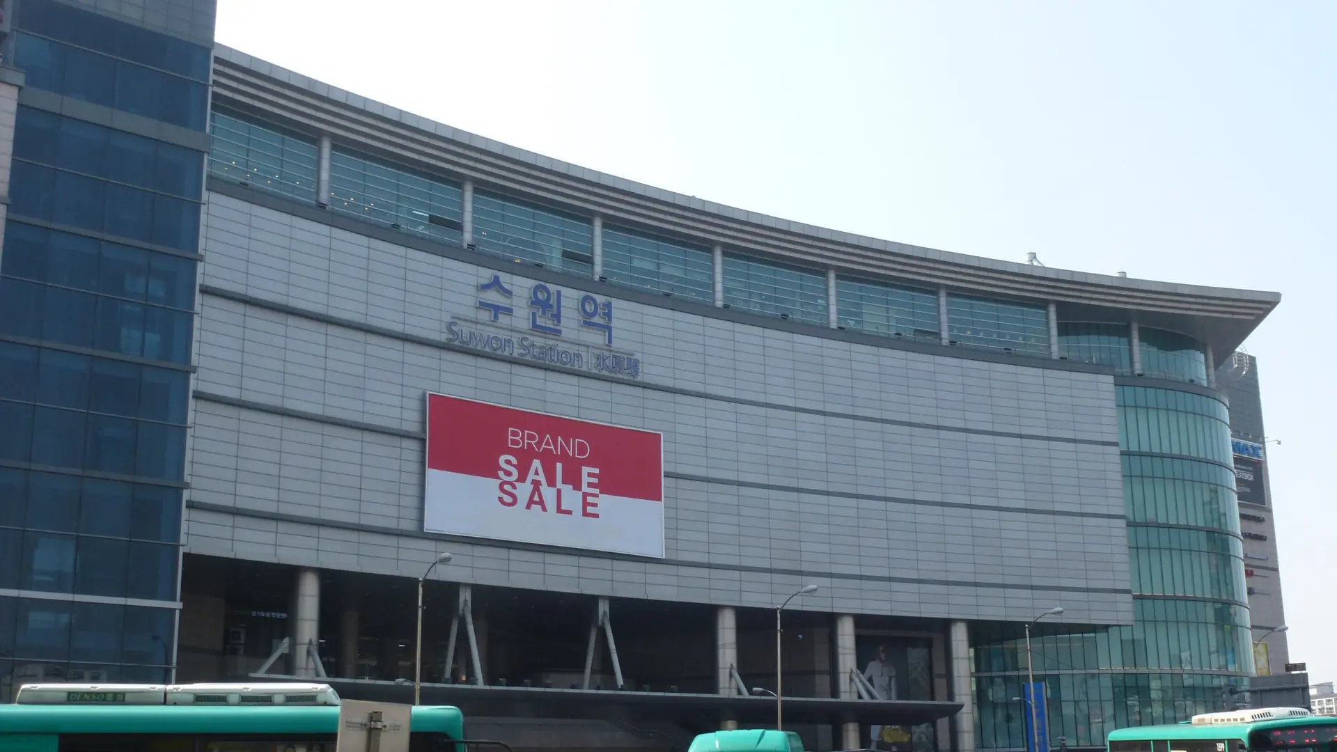 Suwon Station's exterior with its Korean and English signage, buses in front, in bright daylight