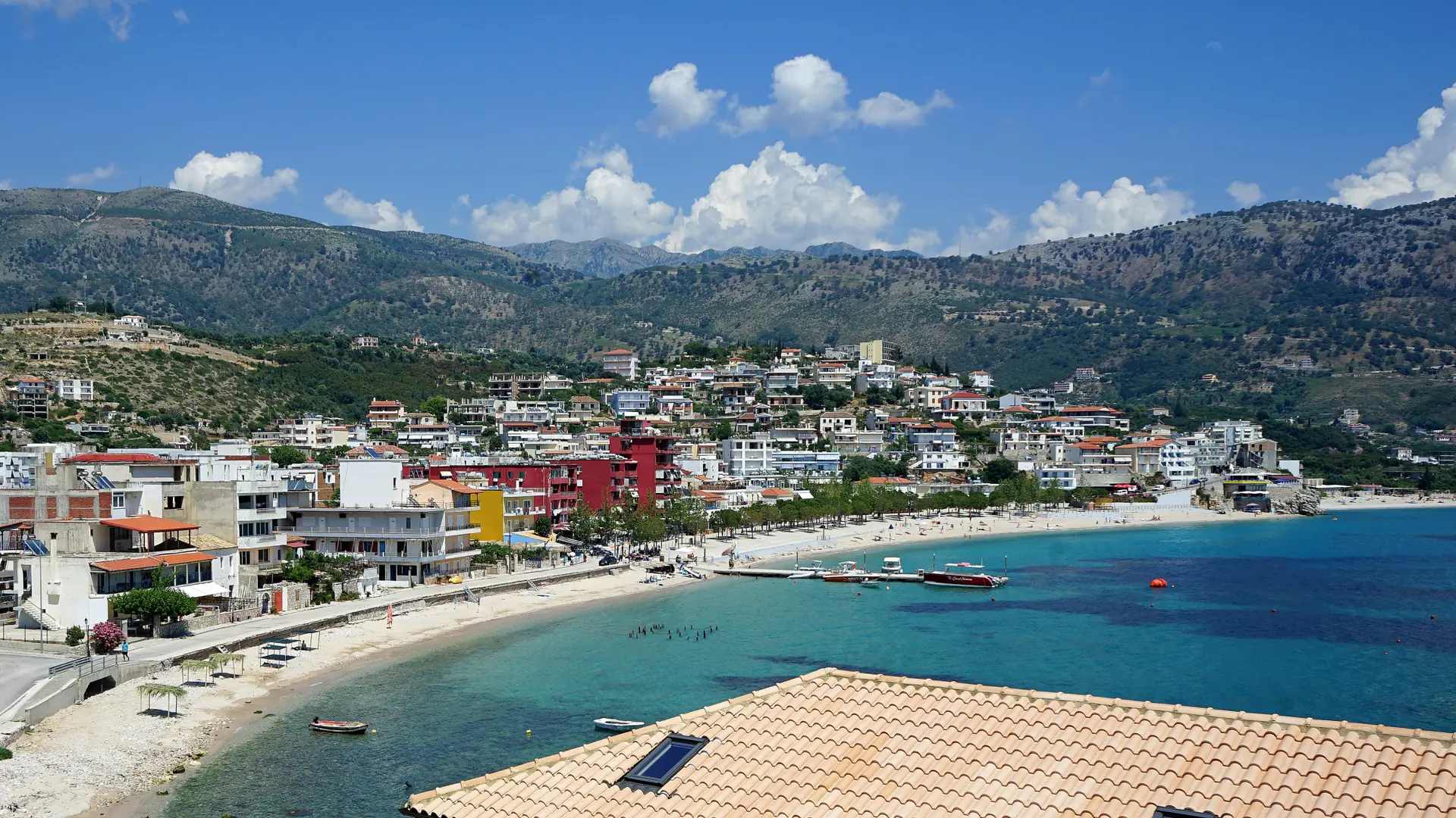 Himarë's town beach and turquoise bay below the mountains on a sunny day