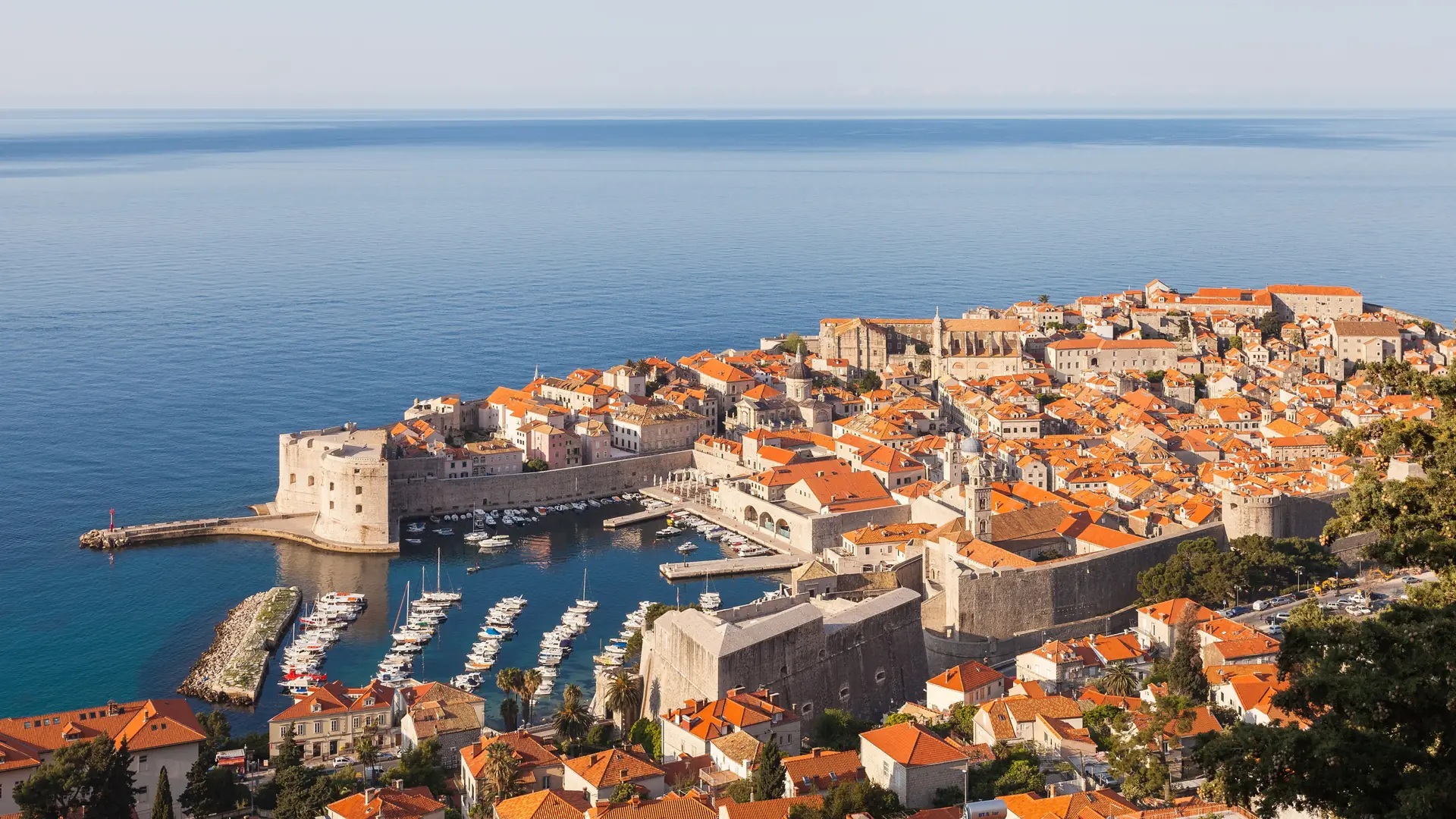An aerial view of Dubrovnik's walled old town, harbour and terracotta rooftops beside the blue Adriatic Sea