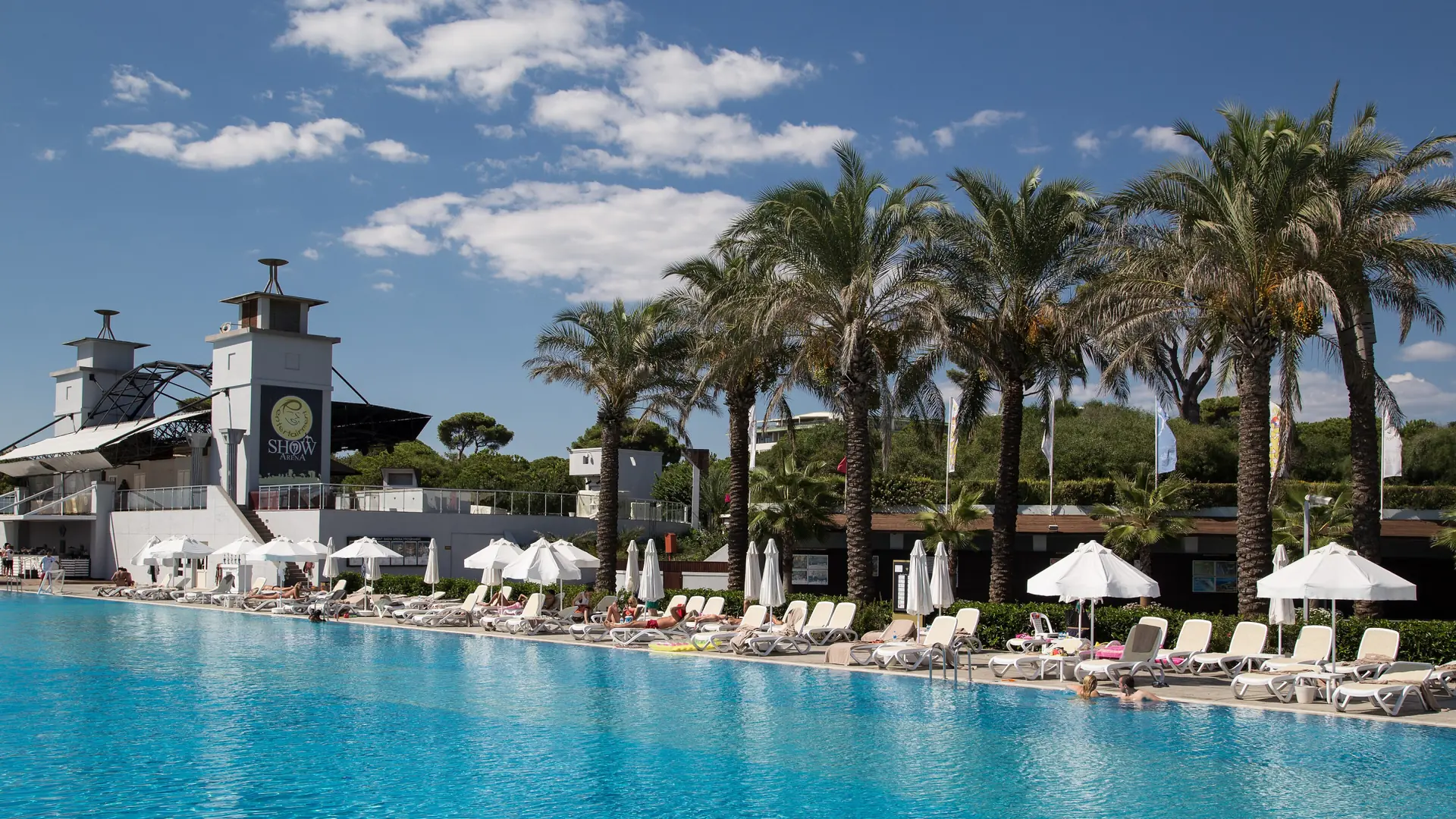Outdoor pool, palms and the Show Arena at Rixos Premium Belek in natural daylight