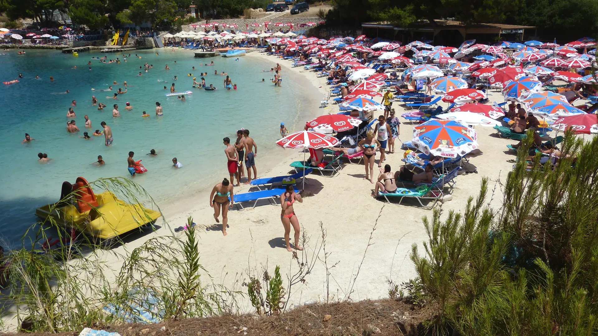 A busy sandy cove in Ksamil with swimmers and closely spaced colourful umbrellas, illustrating the town’s beach setting