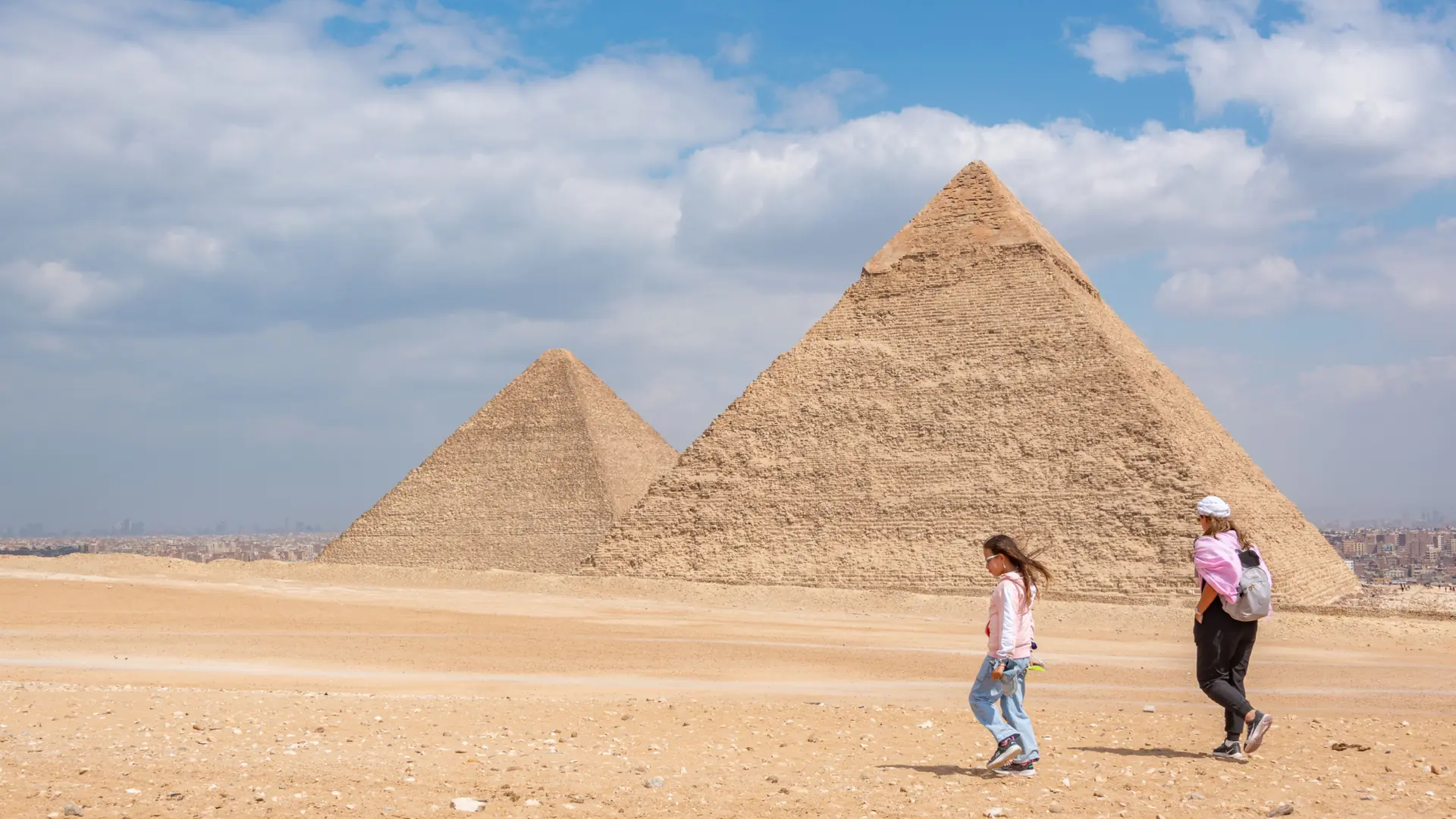 Visitors walking past two Giza pyramids under a bright blue sky