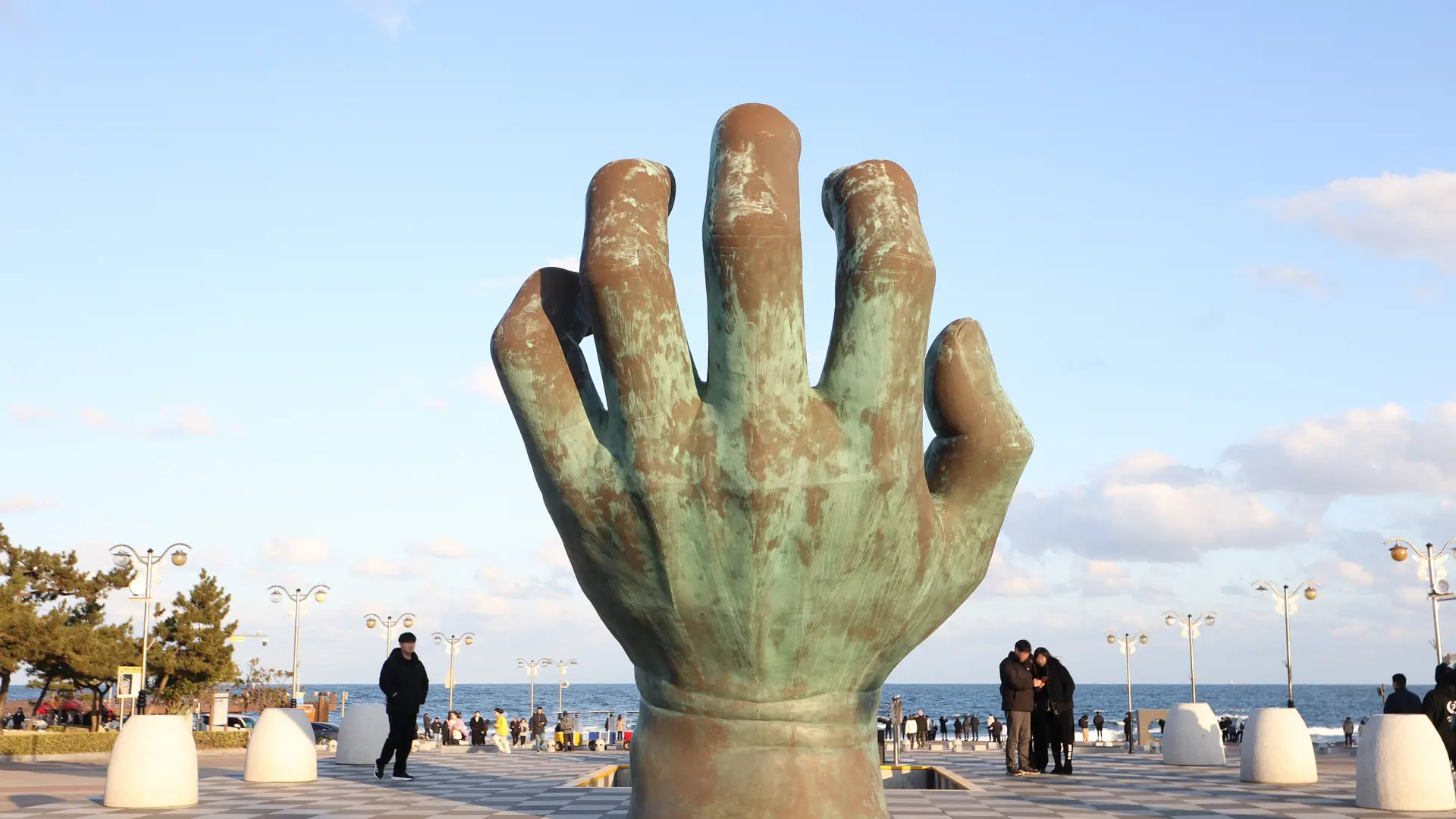 Homigot's giant bronze 'Hand of Harmony' sculpture rising from the sea near Pohang, under a bright sky