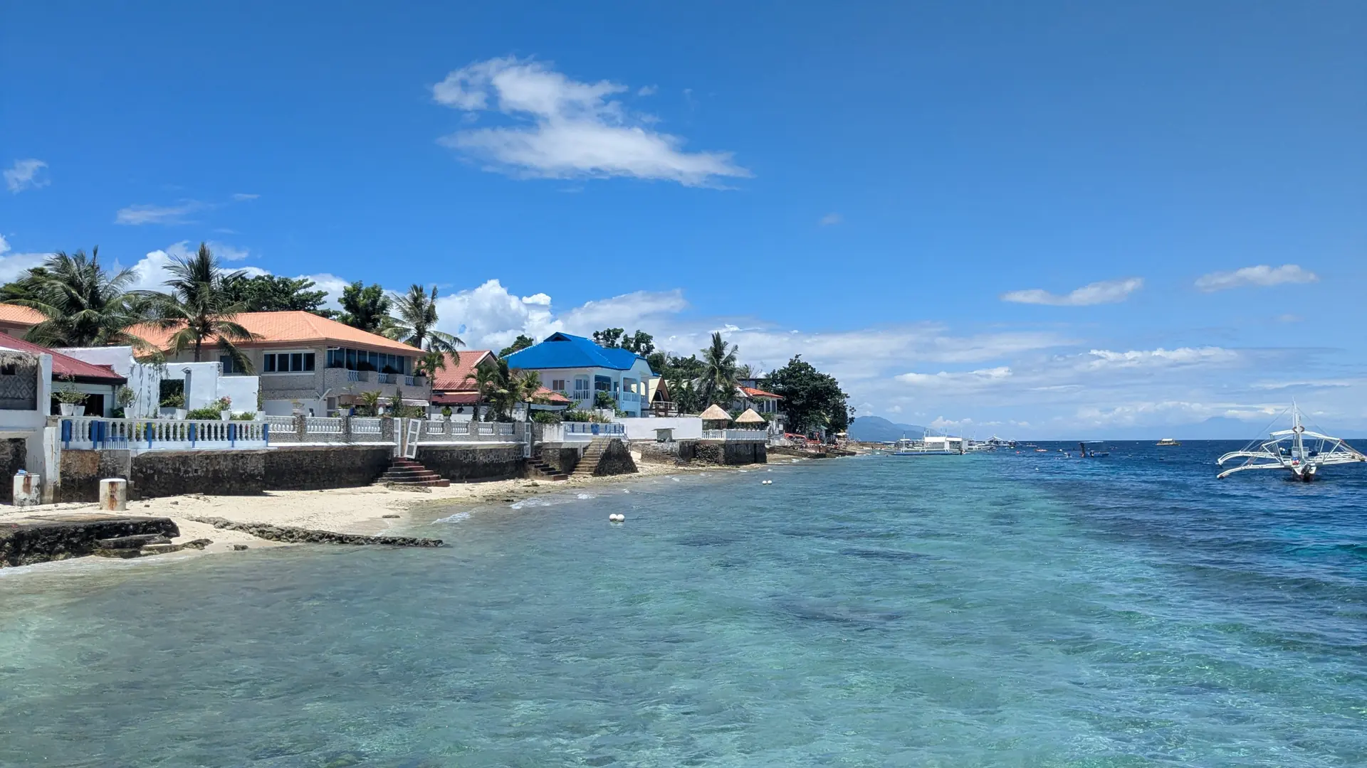 Moalboal’s rocky coastline with waterfront buildings and outrigger boats on blue water