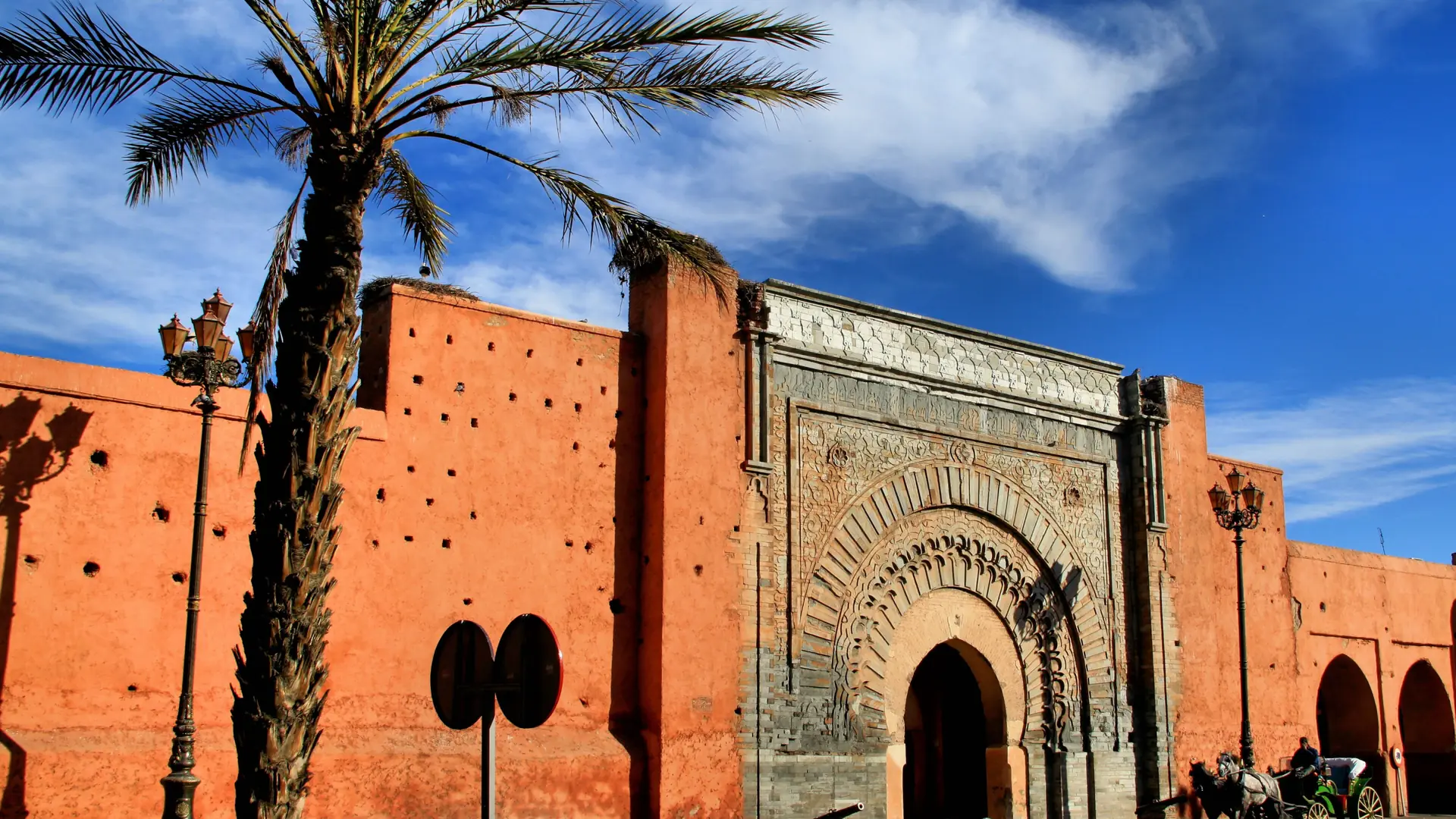 Bab Agnaou gate in Marrakech’s Kasbah, with ochre walls and a palm under blue sky