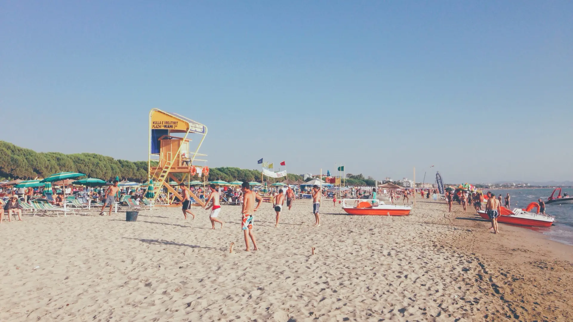 Families, a lifeguard tower and umbrellas on the wide sandy beach at Golem near Durrës on a sunny day