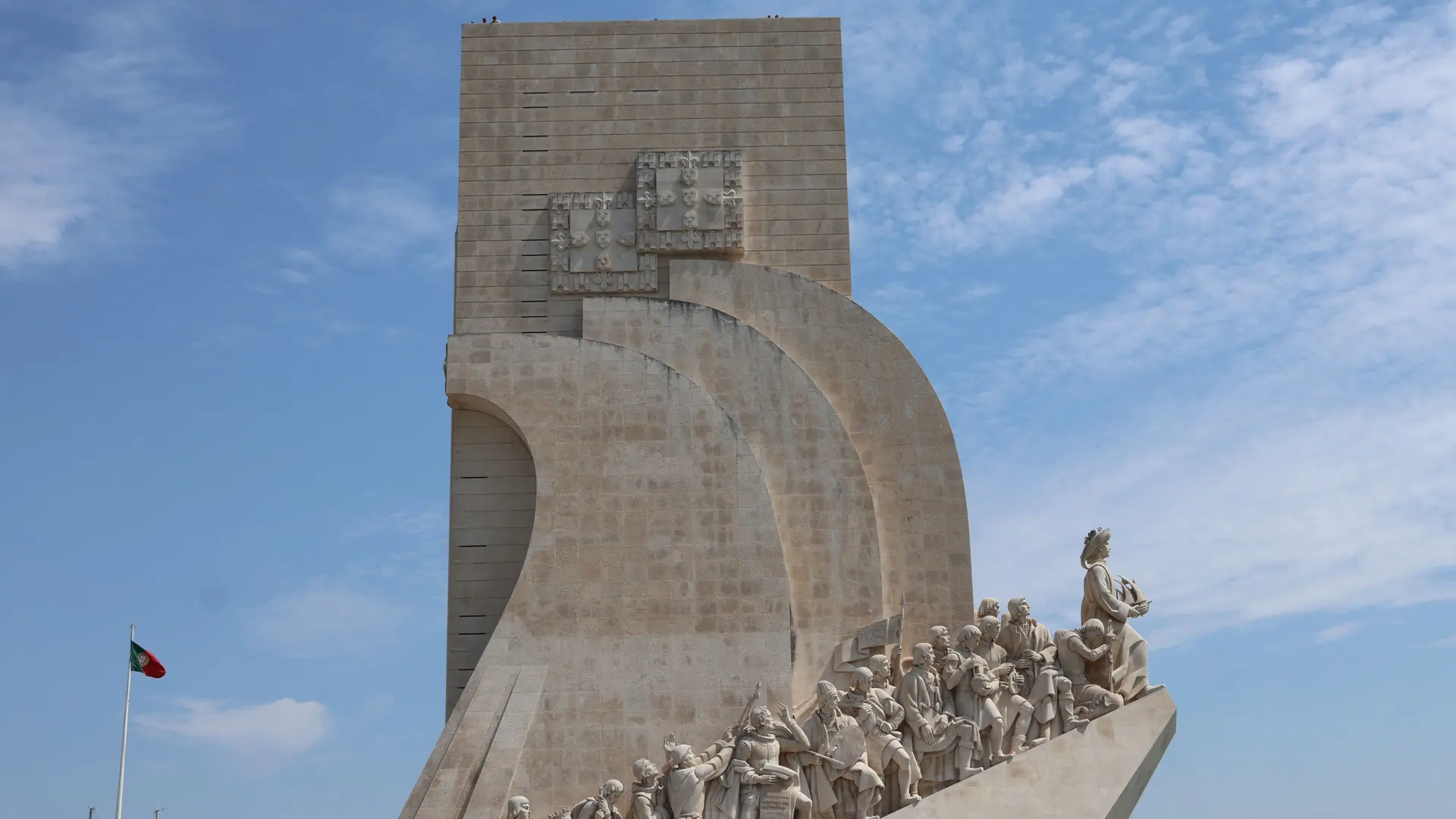 the Padrão dos Descobrimentos monument in Belém, Lisbon, with a Portuguese flag and clear blue sky