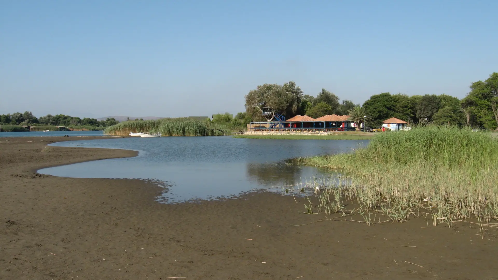 Sandy bank, reeds and low riverside buildings at the Bojana River mouth
