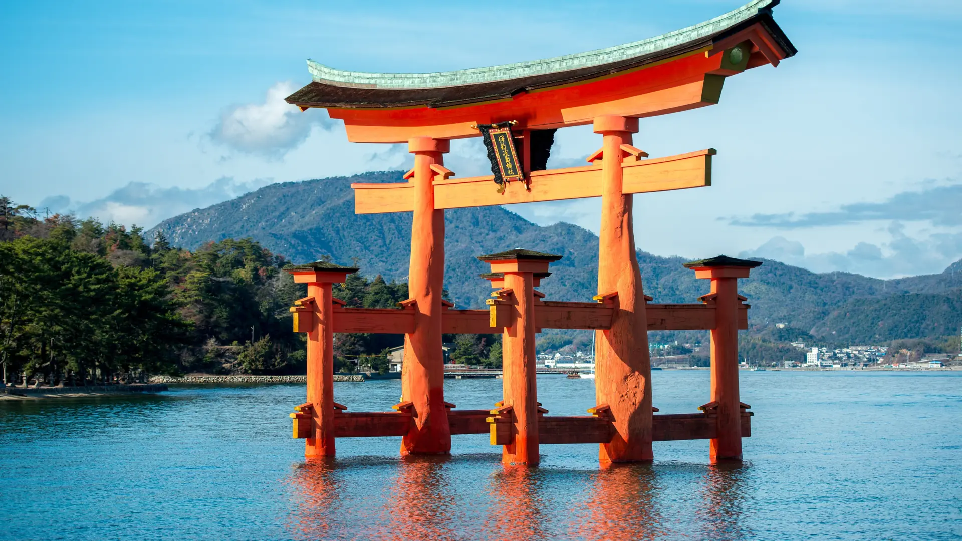 Itsukushima Shrine's red torii standing in blue water off sunny Miyajima island