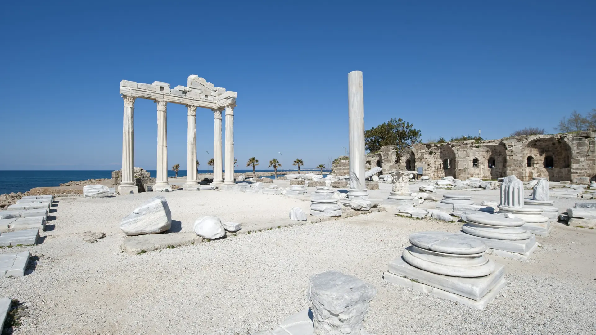 Sunlit Temple of Apollo columns and coastal ruins, shown as a wider Side city scene