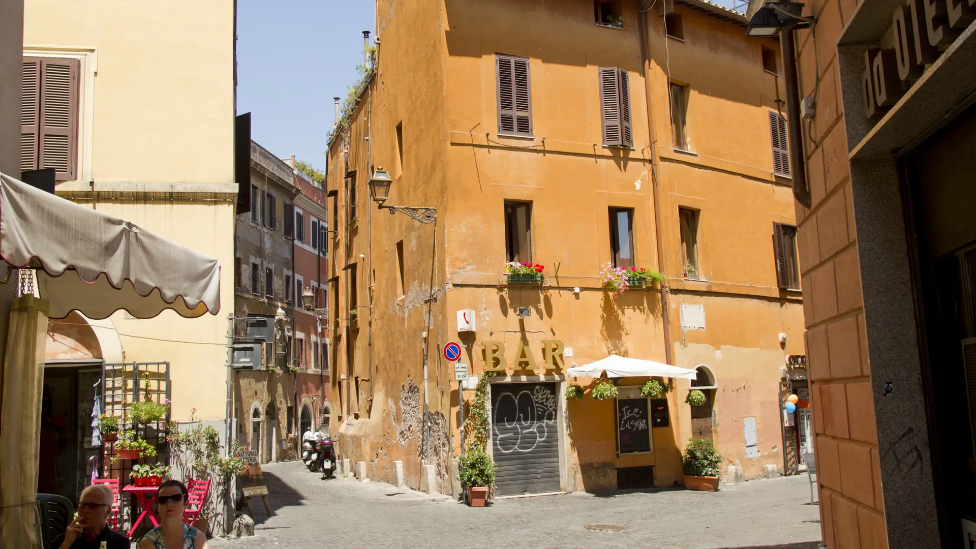 a sunlit terracotta corner in Trastevere, Rome, with a bar terrace and café tables