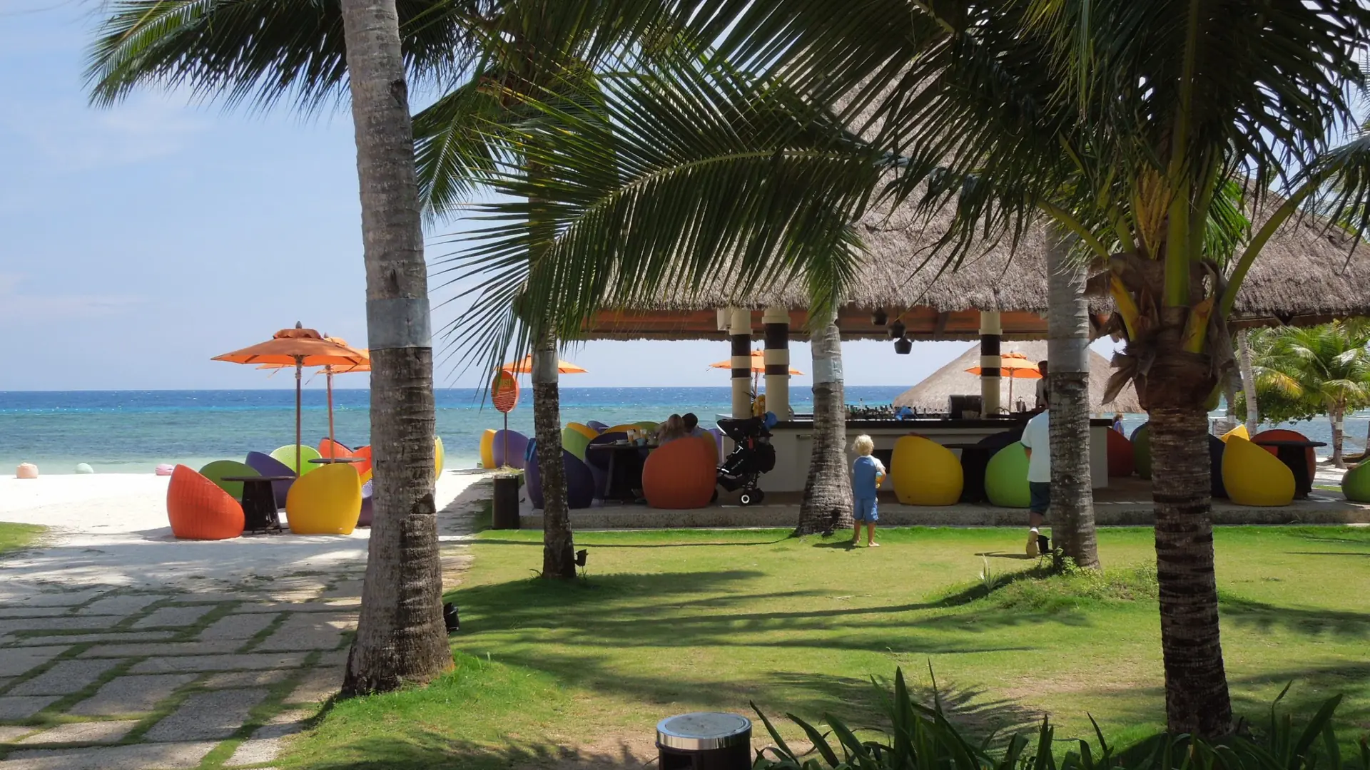 Coloured beanbags beneath palms beside a thatched beach bar facing turquoise water in Bolod, Panglao