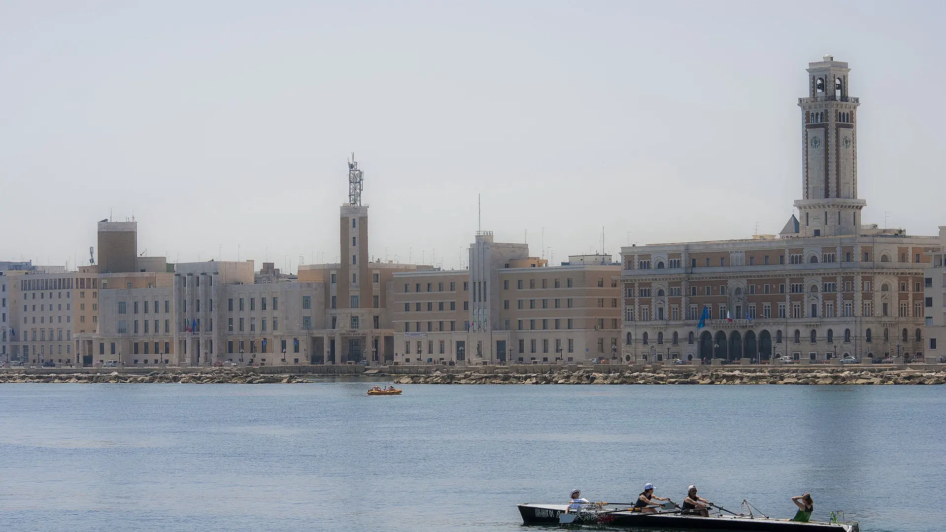 rowers on the calm water off Bari's lungomare with the clock tower skyline behind