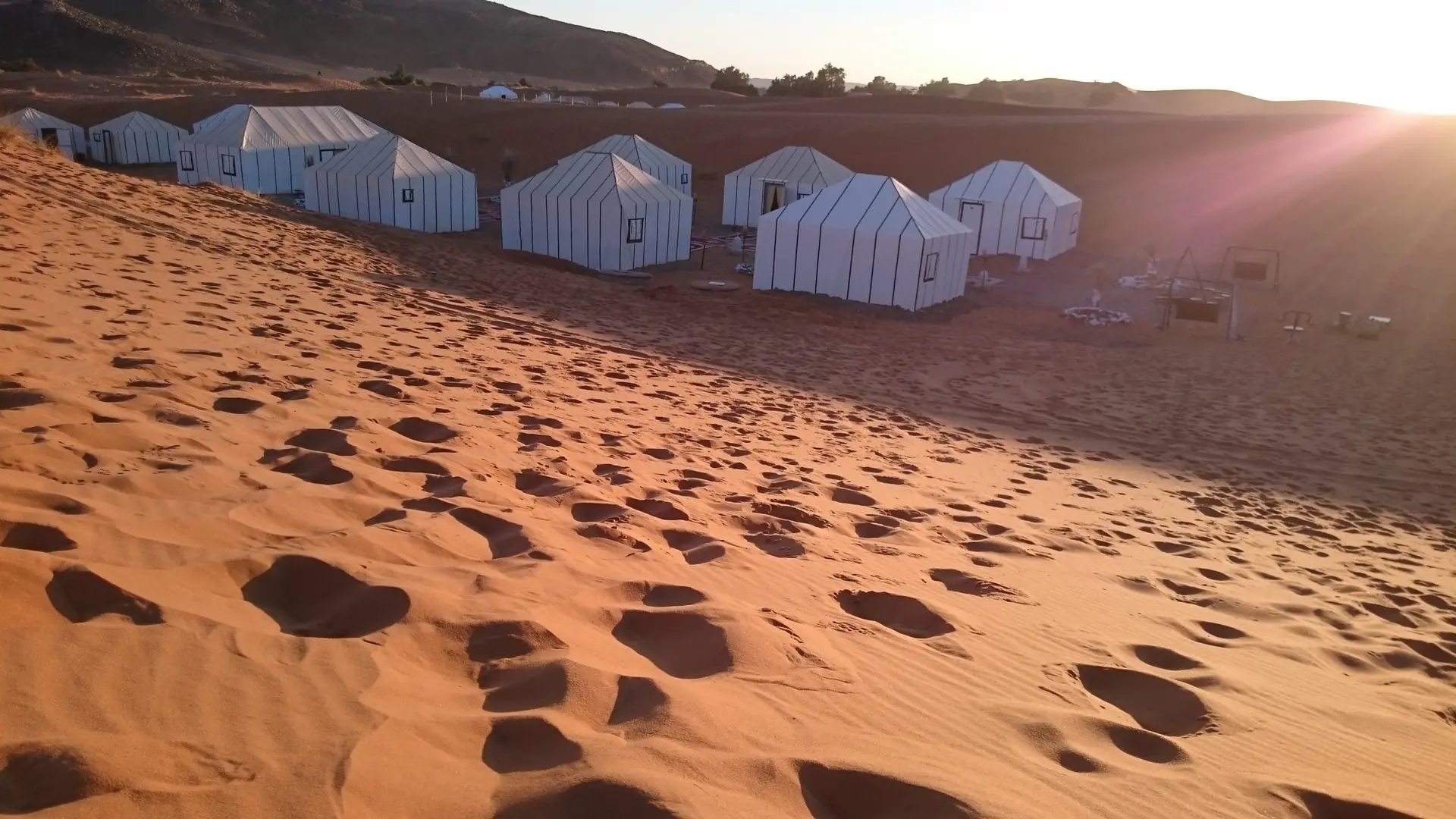White desert camp tents among the orange dunes near Merzouga in daylight