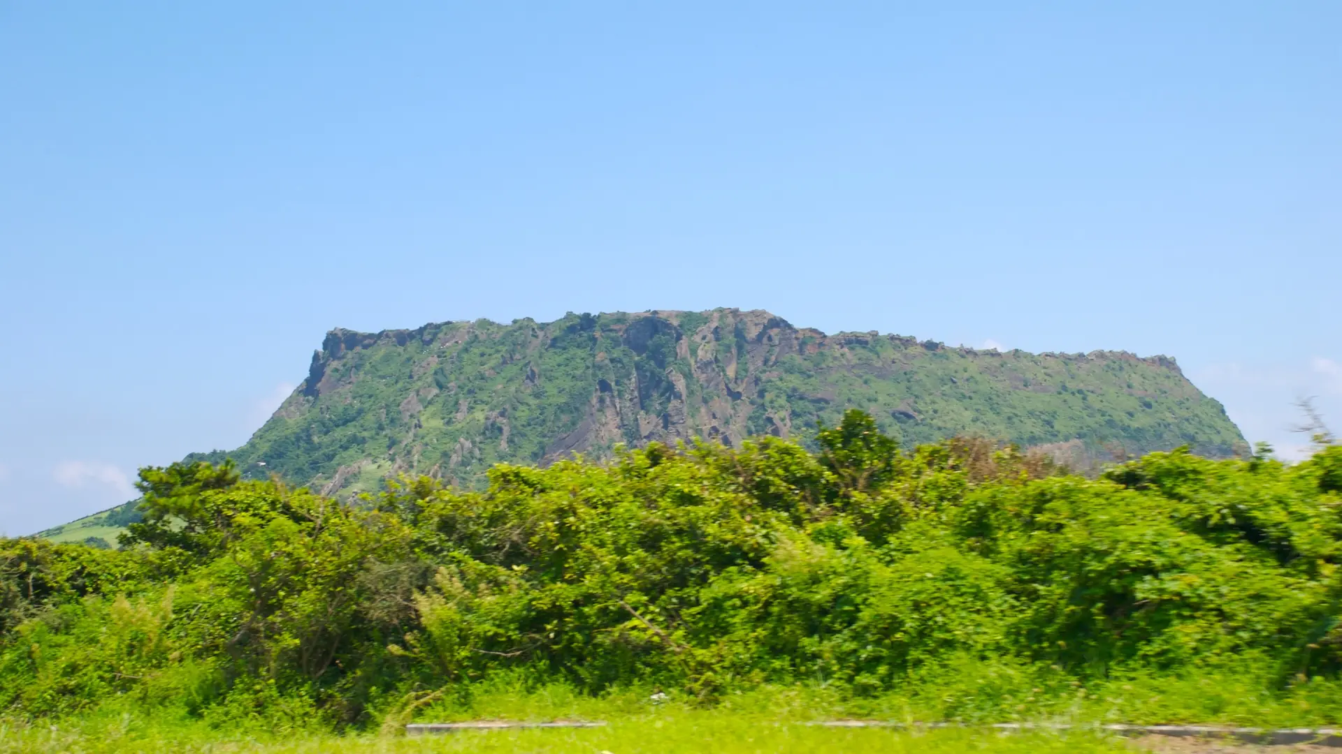 Seongsan Ilchulbong's green volcanic tuff cone rising above the Jeju coastline under a clear blue sky