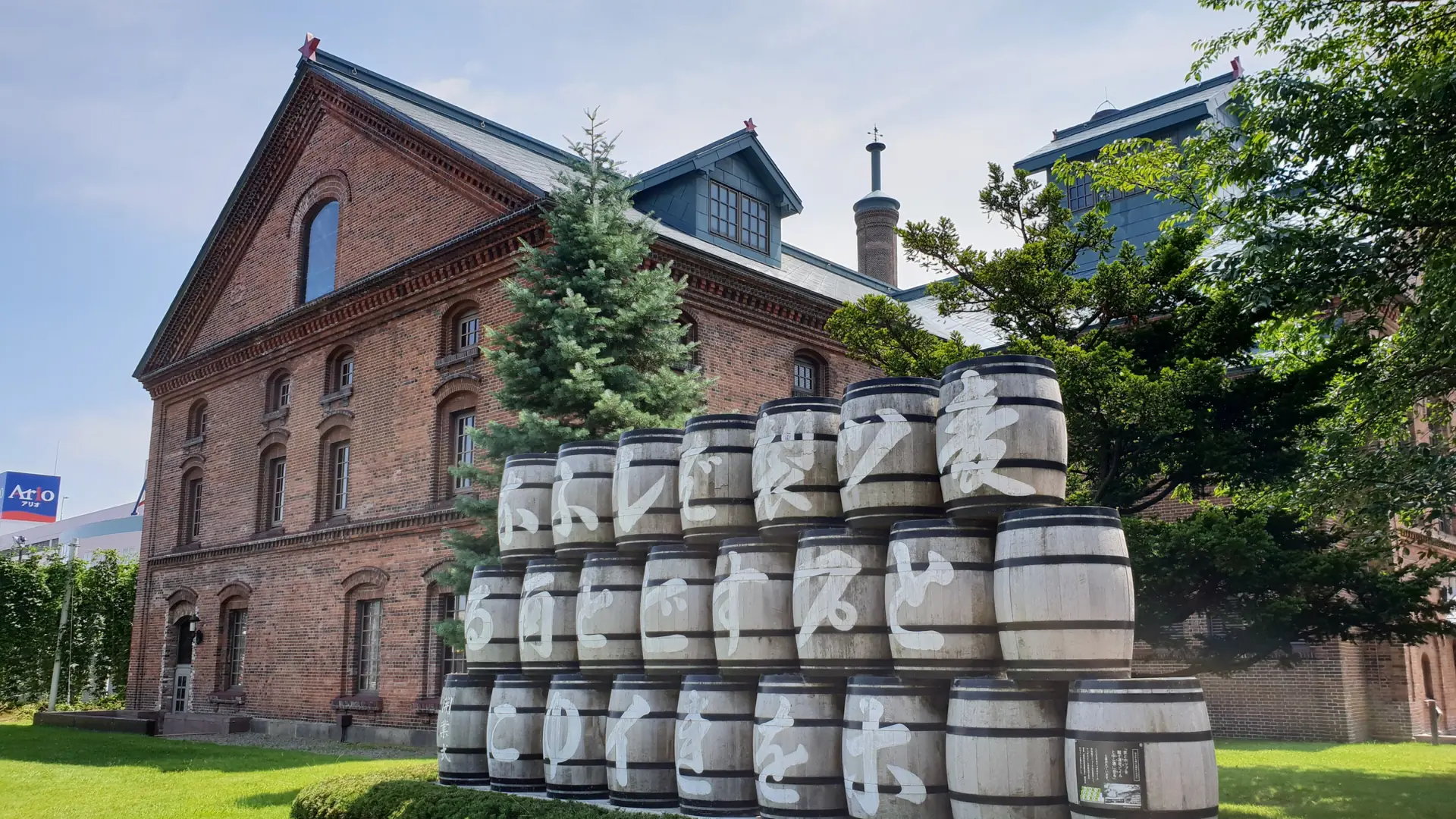 Wooden beer barrels on the sunny lawn beside Sapporo Beer Museum’s red-brick building