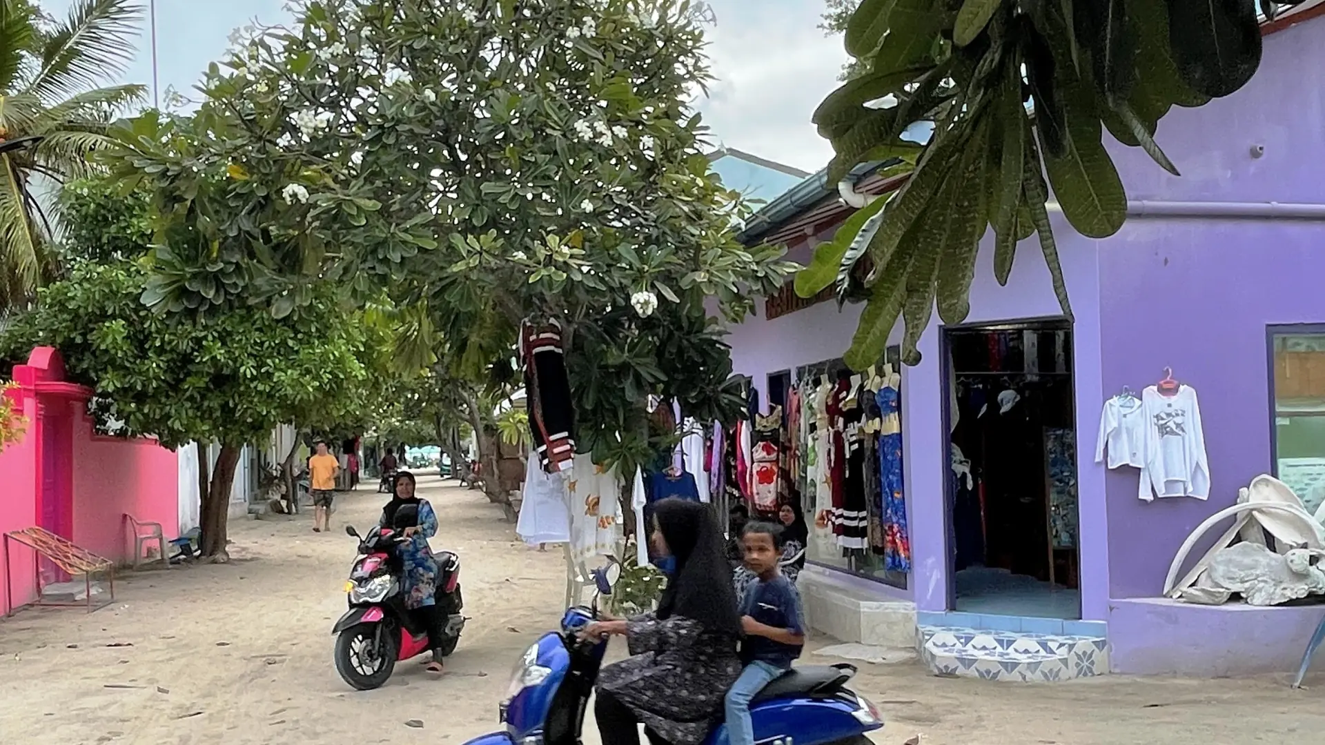 Shops and people at a sandy street intersection on neighbouring Dhangethi island
