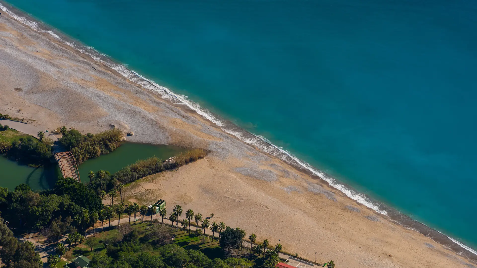 Wide sandy Aegean shoreline and turquoise water seen from above in bright daylight
