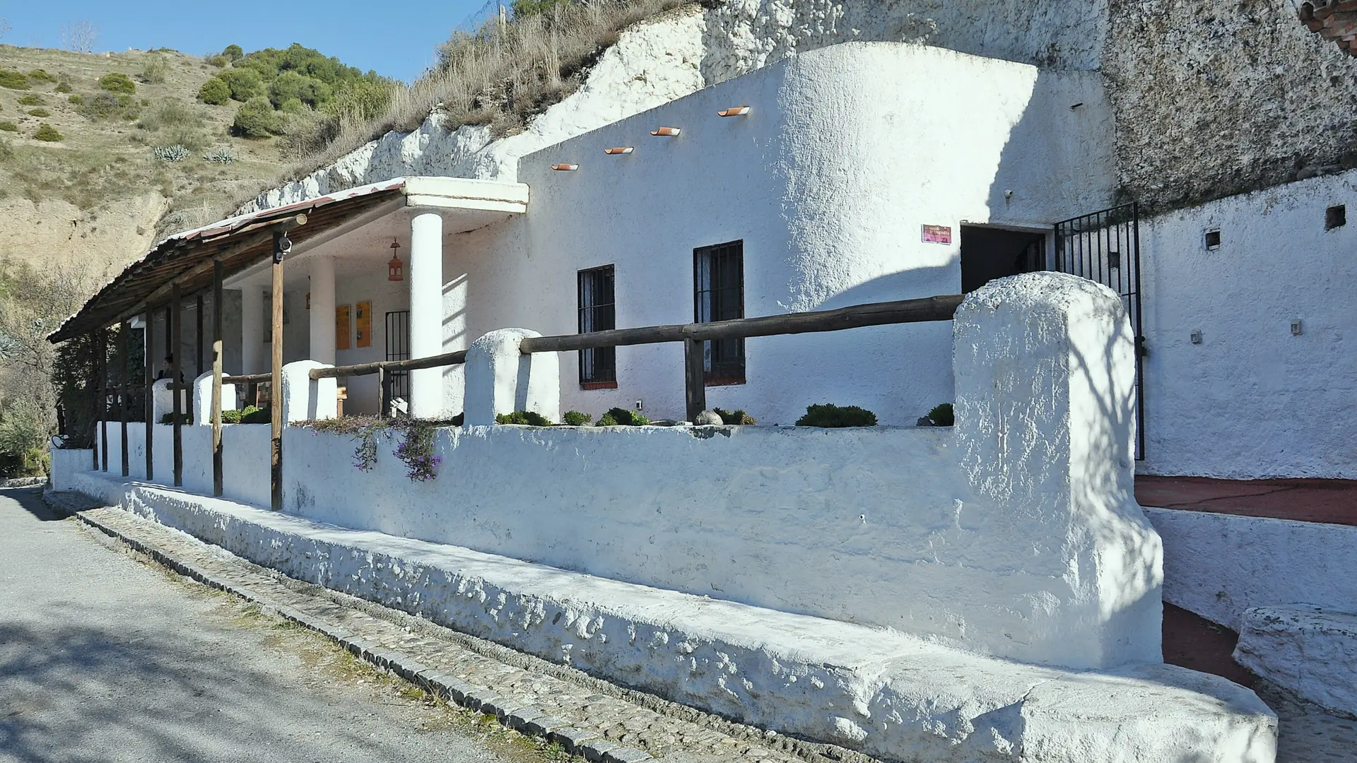 Sunlit white cave buildings and wooden veranda at Museo Cuevas del Sacromonte, Granada