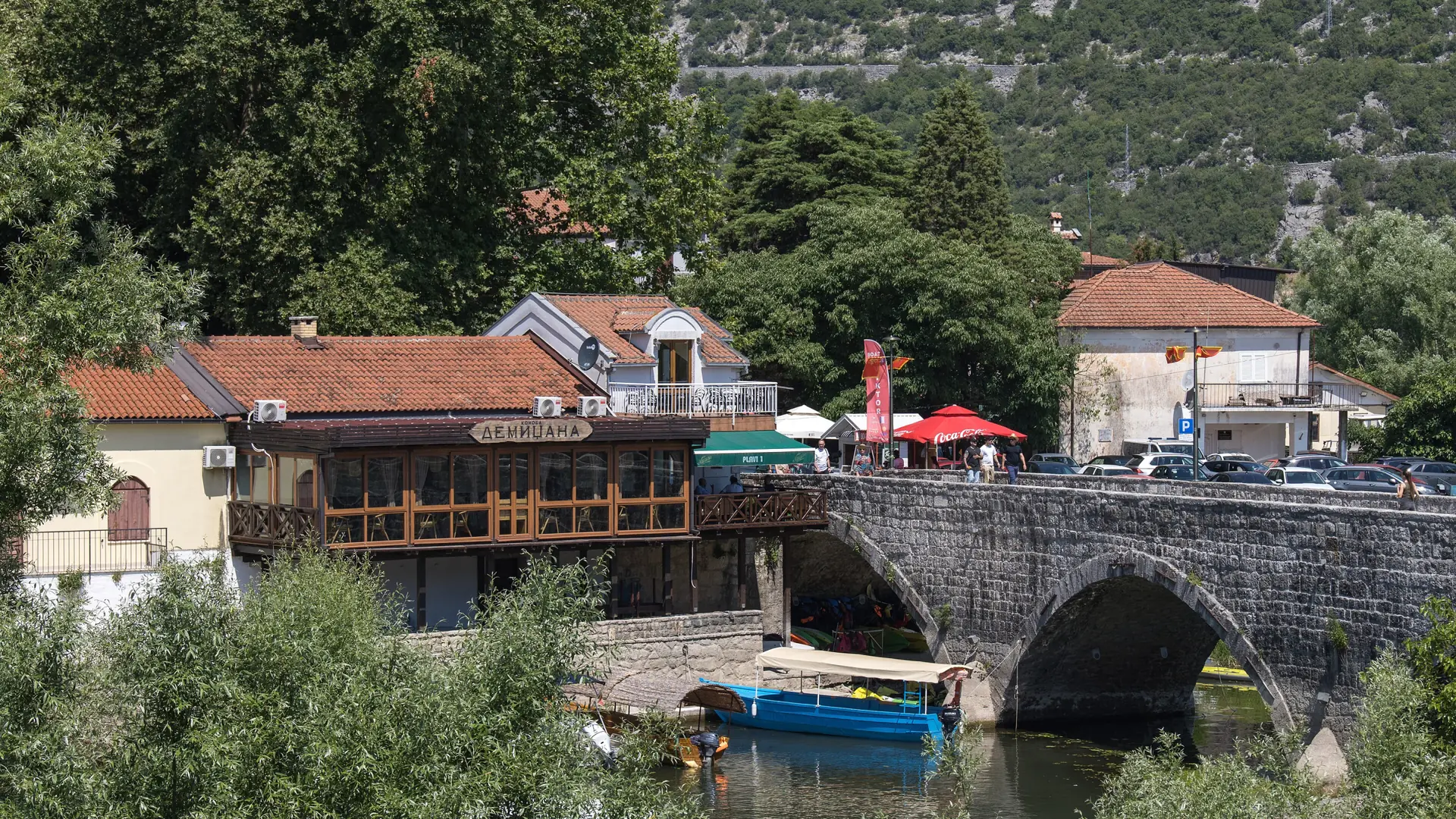 Tour boats moored beneath Virpazar's stone bridge beside green water in daylight