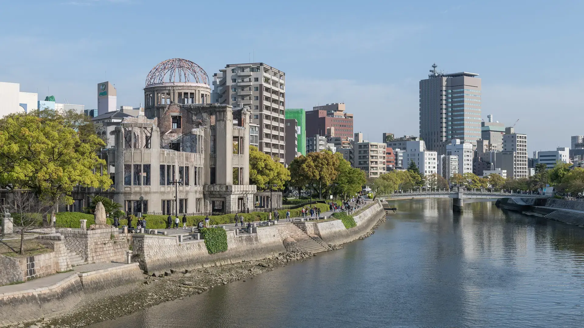 Atomic Bomb Dome beside the green riverbanks of central Hiroshima under a bright sky