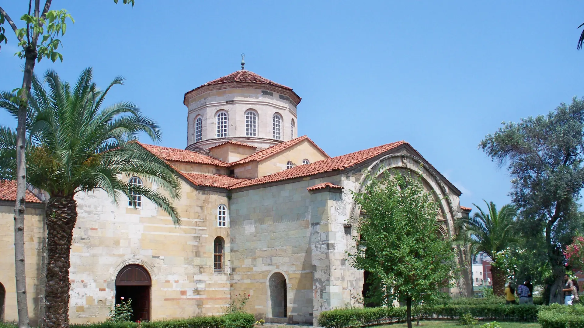 Sunlit Hagia Sophia of Trabzon with its red tiled dome and garden, shown as a wider city scene