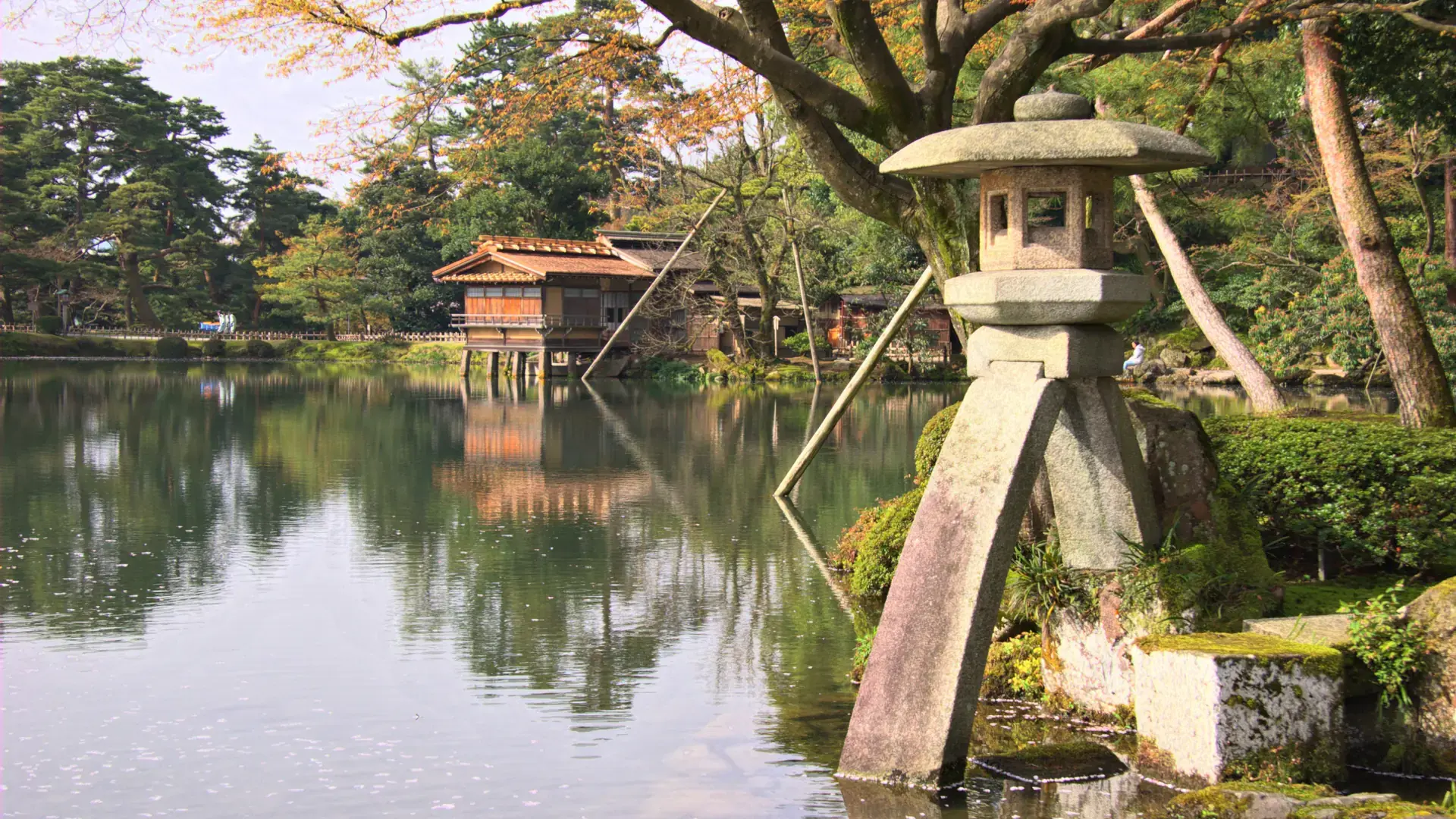 Kenrokuen Garden's Kotoji lantern beside blue water and sculpted pines in bright sunshine