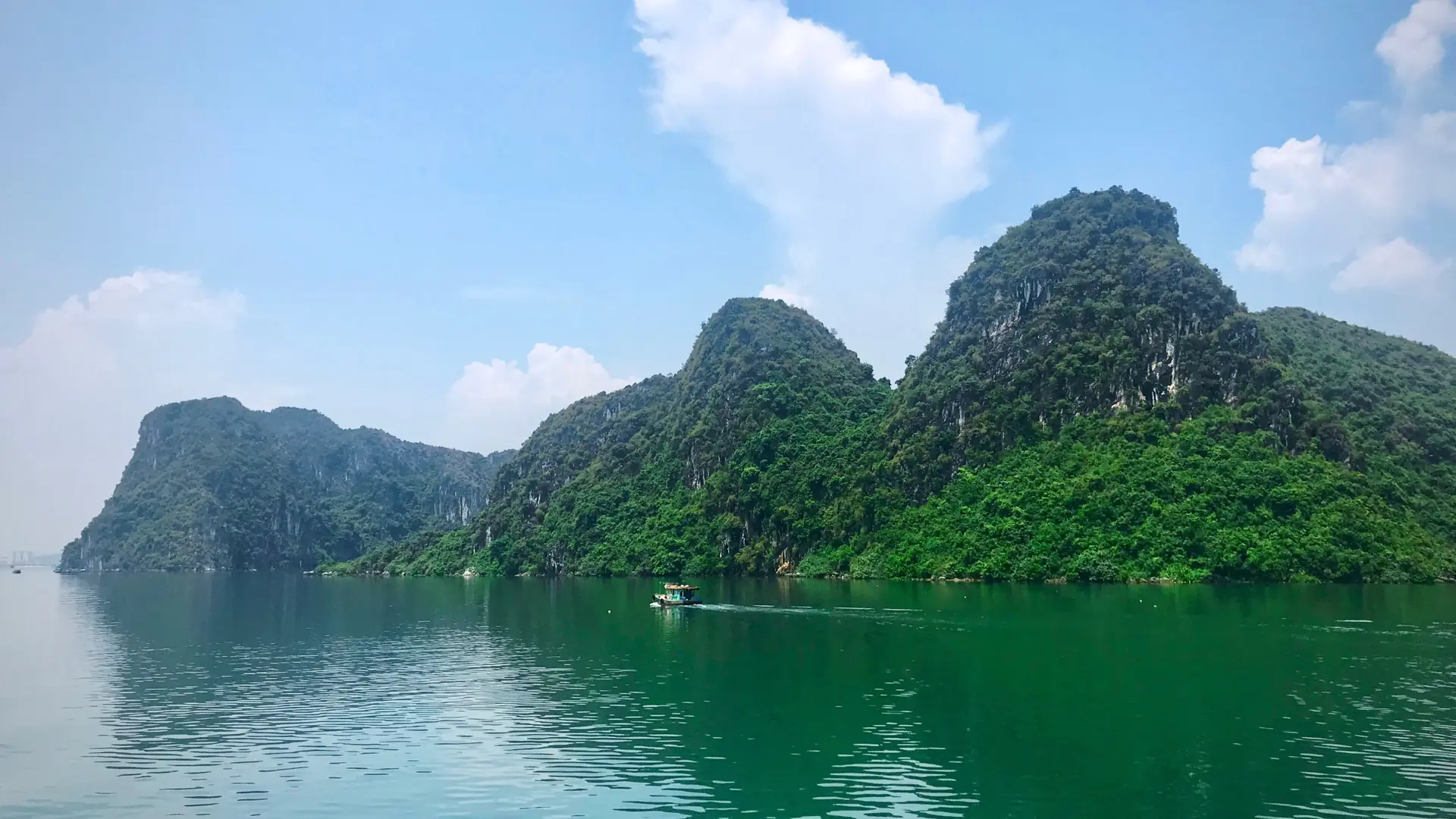 Green limestone cliffs and a small boat in the wider Ha Long Bay landscape.