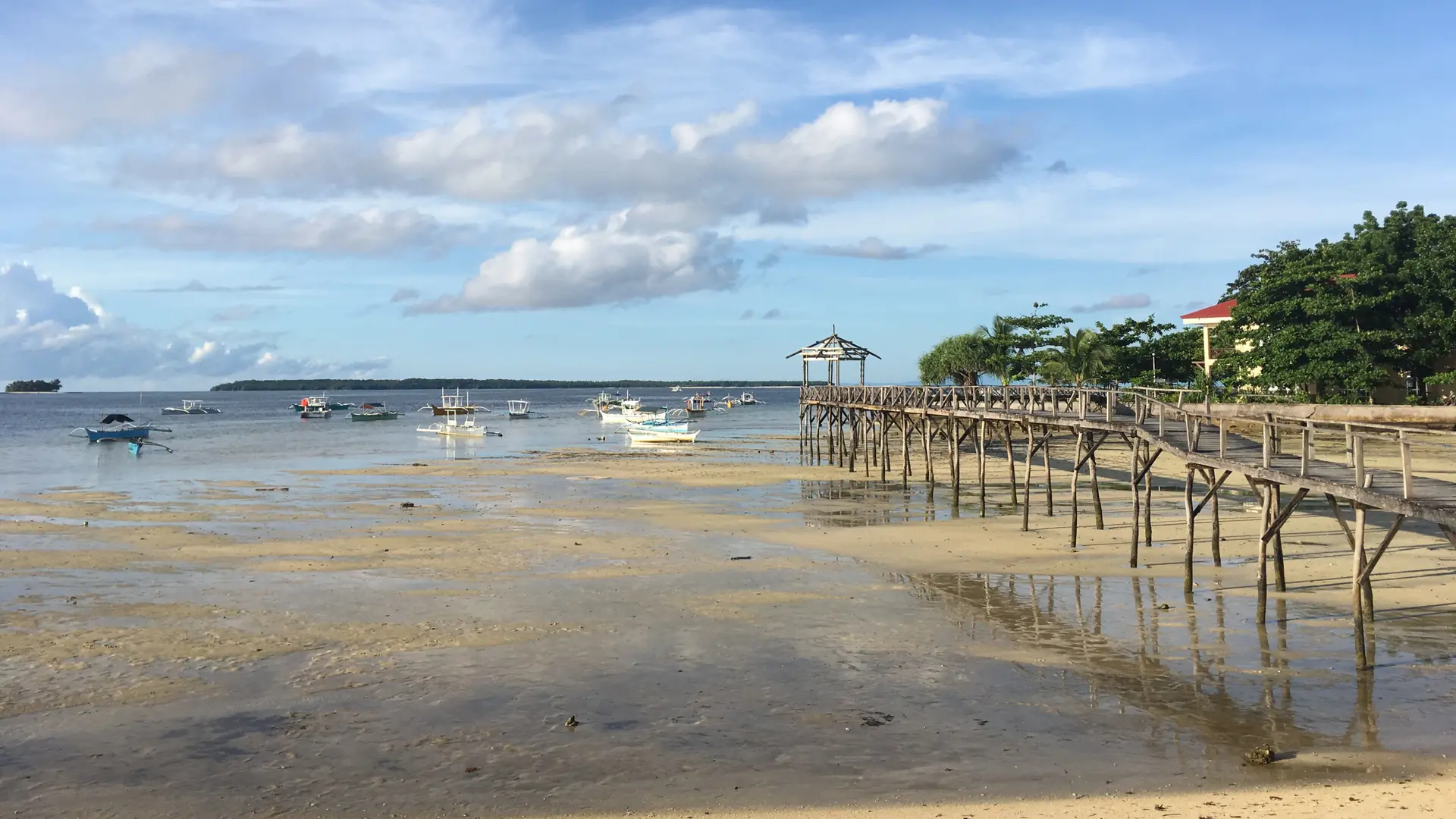Boats and a wooden pier along General Luna’s sandy shore at low tide, Siargao