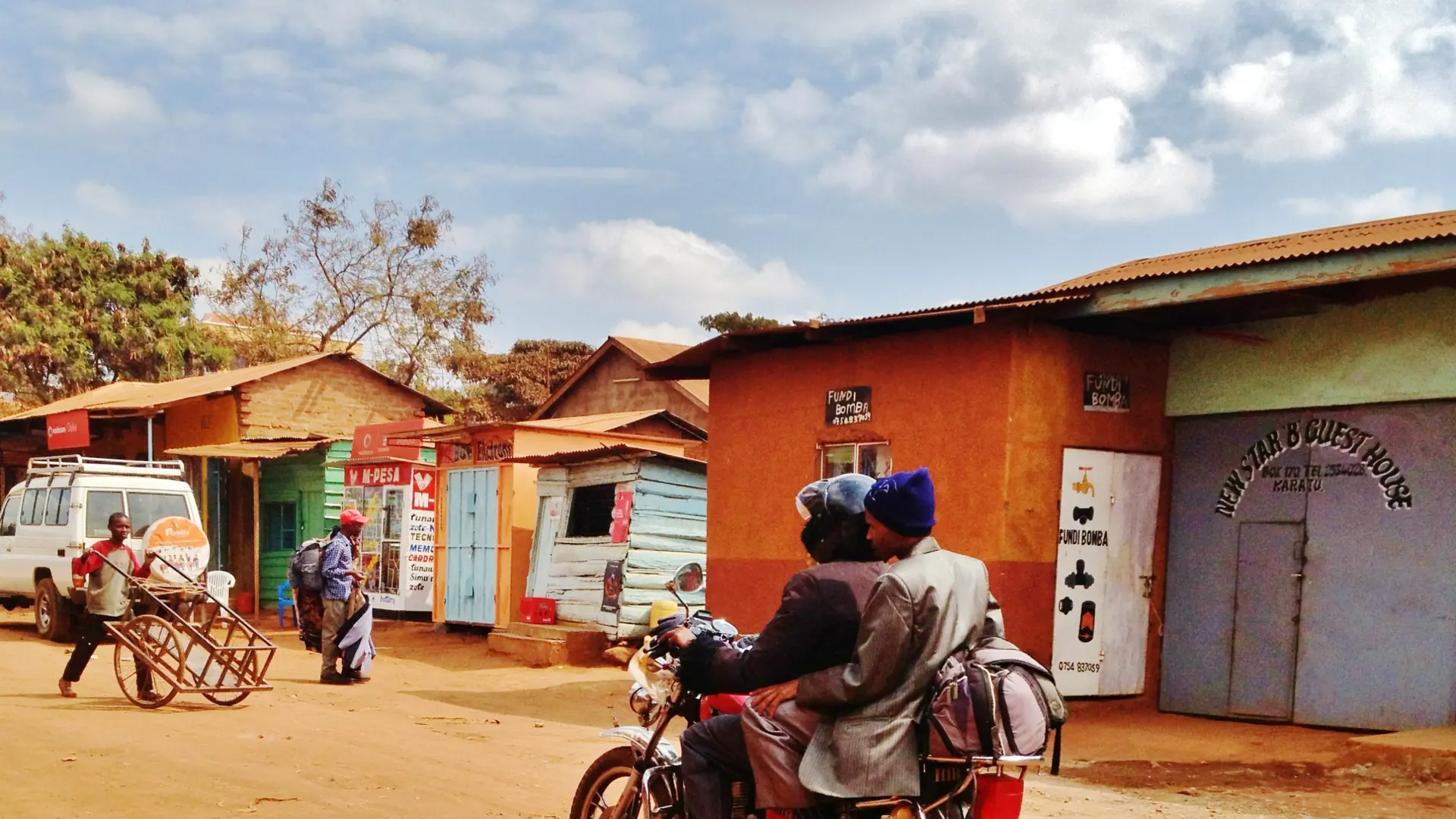 Sunlit Karatu street with a motorcycle and bright shopfronts in northern Tanzania