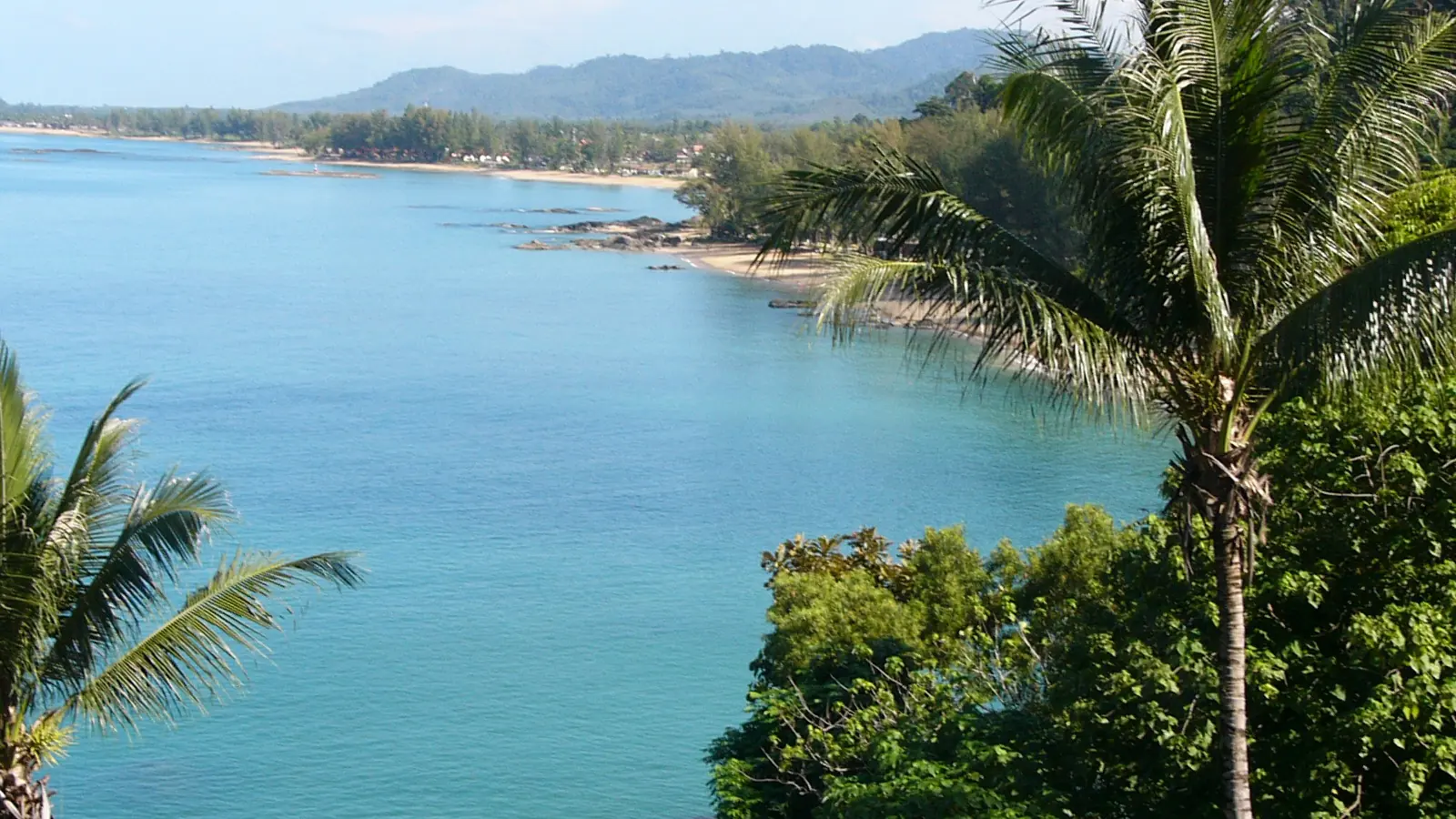 Blue Andaman water curving past palms and green hills at Khao Lak