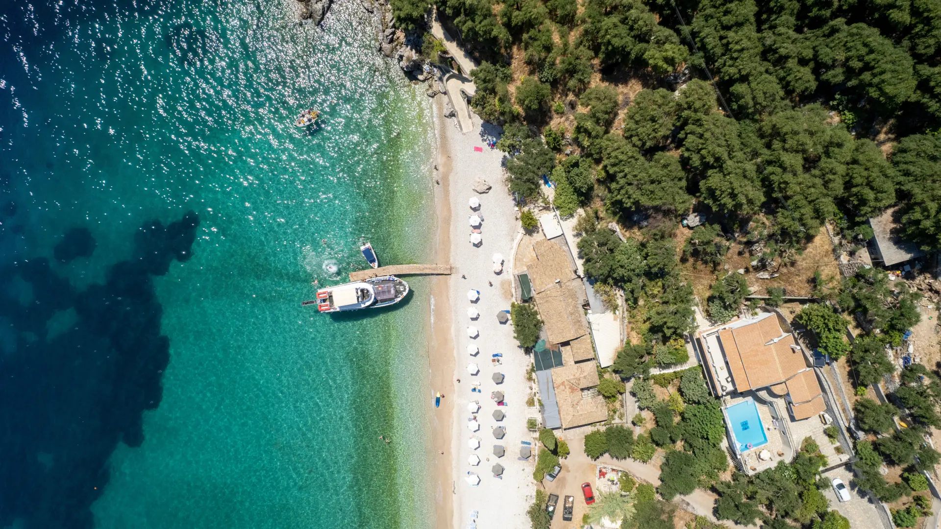 Aerial view of a turquoise Skiathos beach edged by dense green pine forest