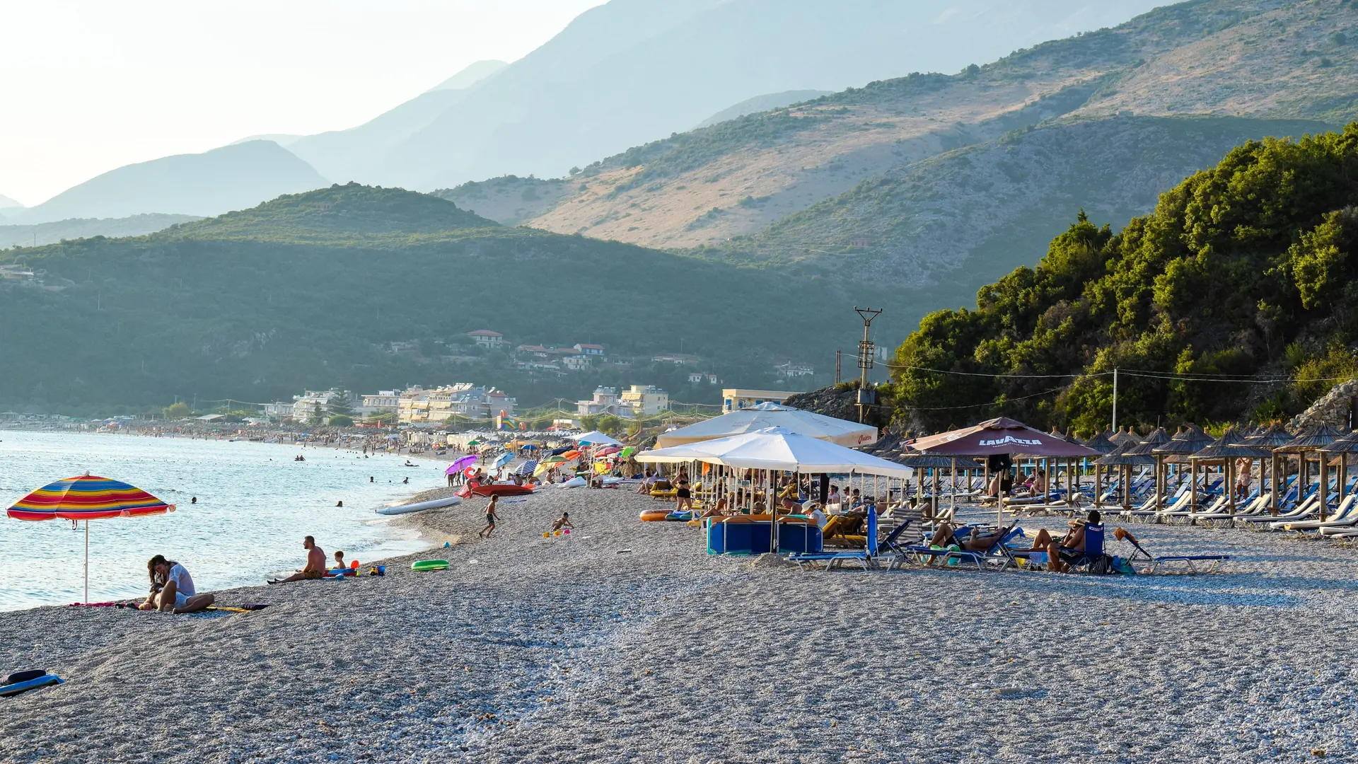 The long pebble beach of Livadh near Himarë with clear blue water and green slopes behind