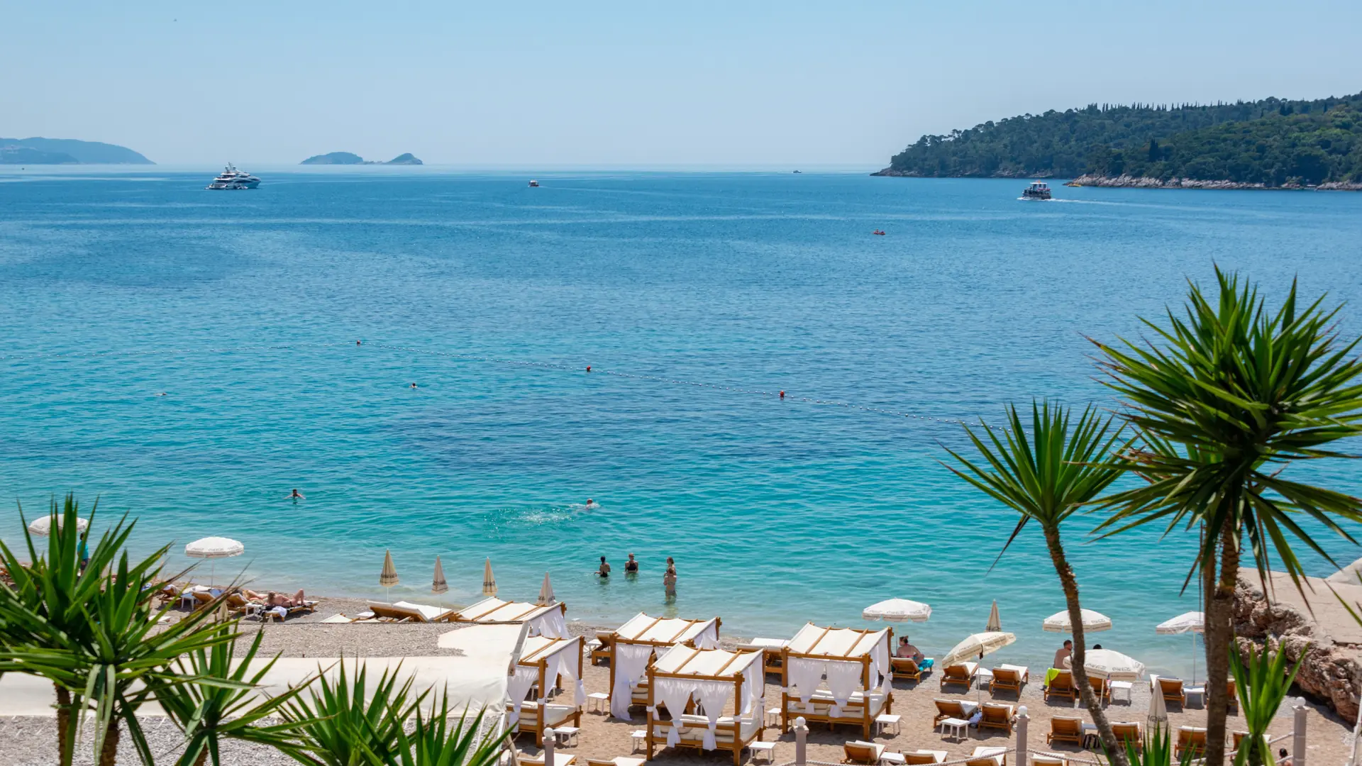 Sunny Lapad Bay promenade with pines, calm blue water and Dubrovnik hotels