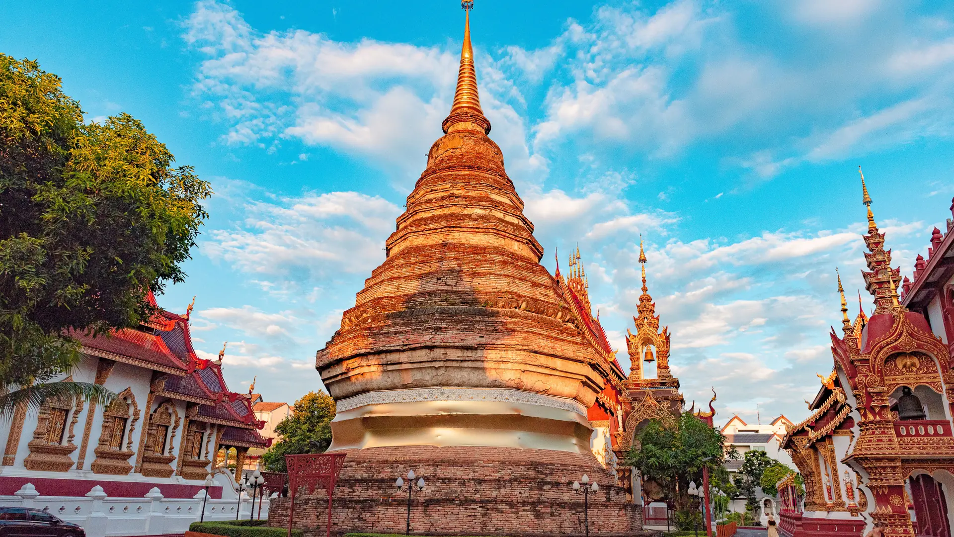 Golden chedi and timber temple halls in a green Chiang Mai courtyard