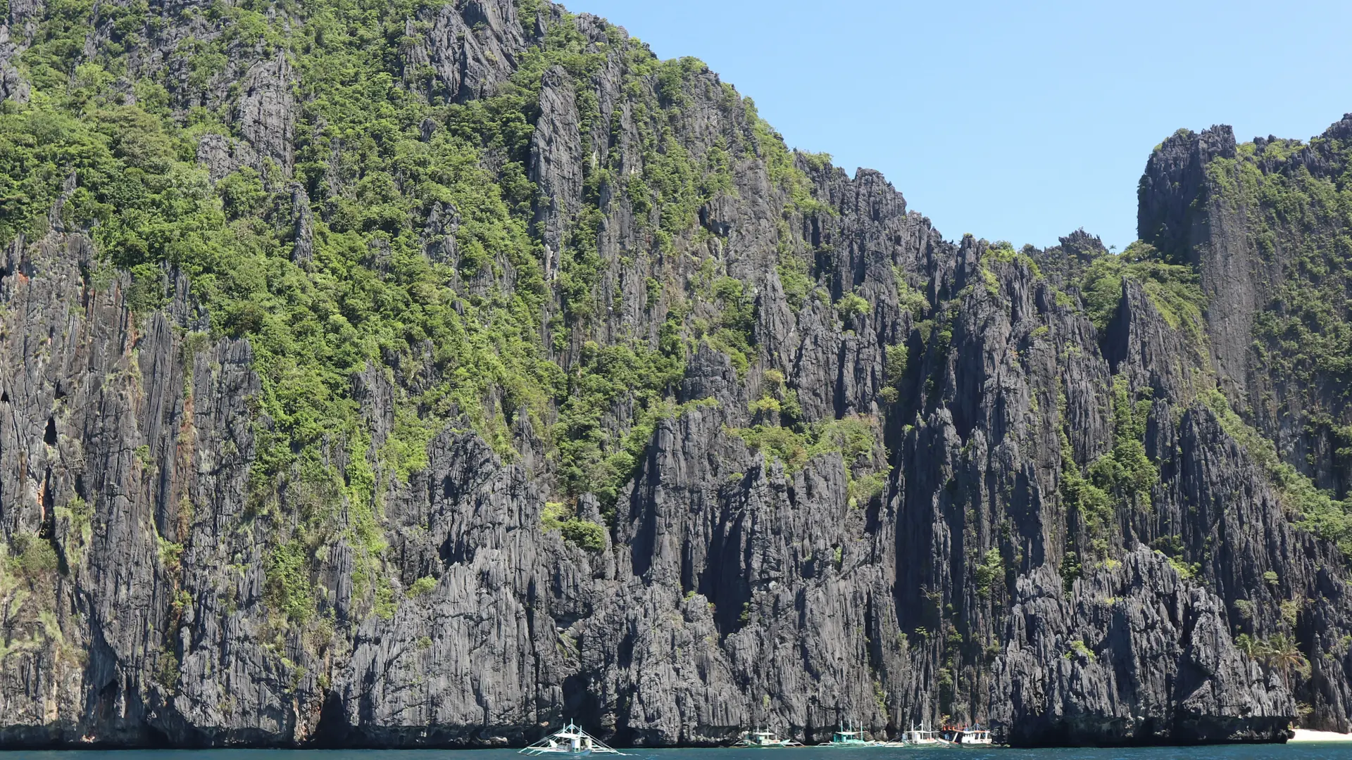Boats beneath grey limestone cliffs and green forest on Miniloc Island, El Nido