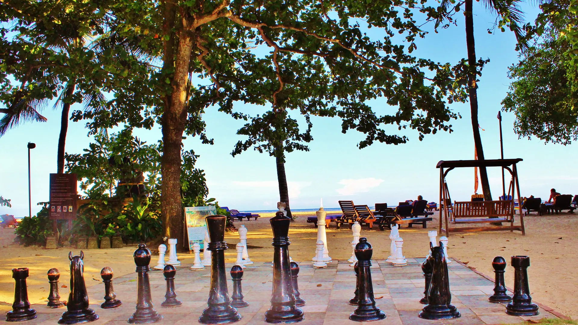 An outdoor chess set and loungers beneath trees beside Sanur’s beach