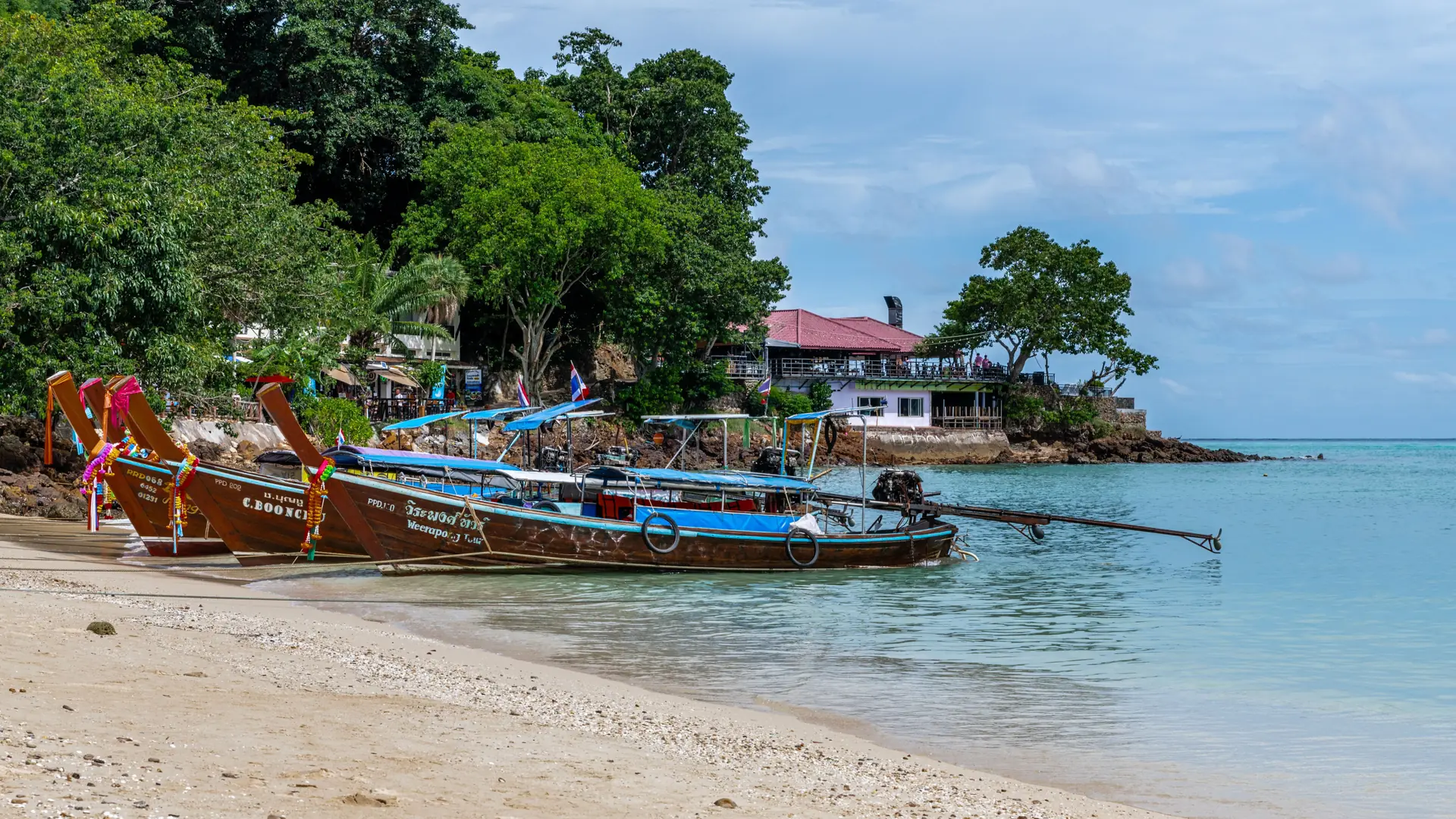 Small boats moored in calm water off Phuket's sandy shore
